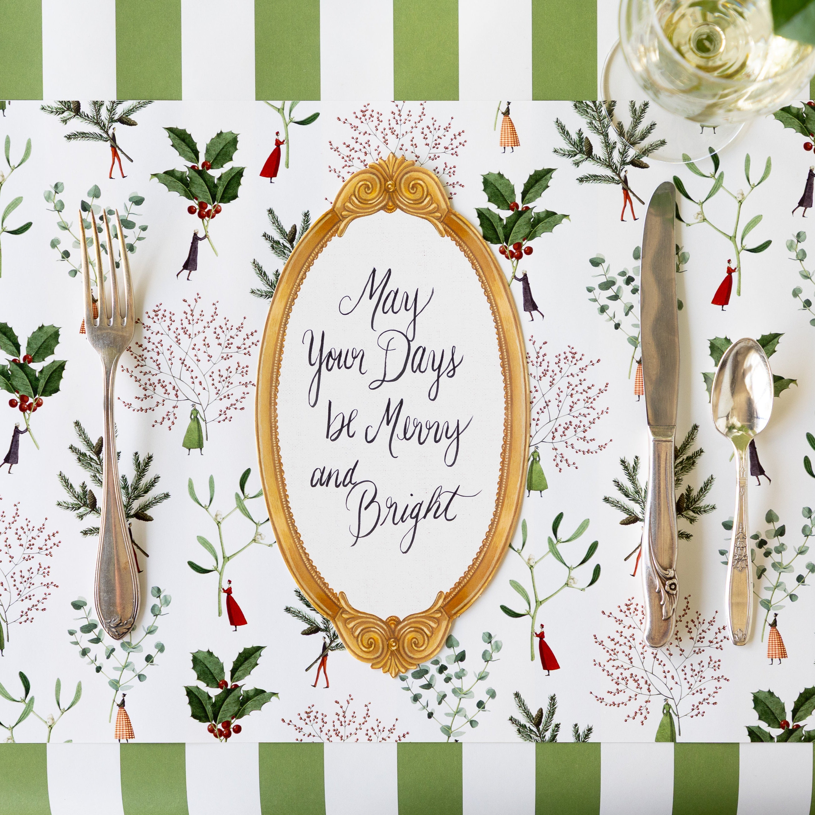 A place setting featuring the Happy Christmas Placemat with vintage silverware, a glass of wine, Antique Gold Frame Table Accent reading "May Your Days be Merry and Bright" atop, and Moss Classic Stripe Runner underneath.