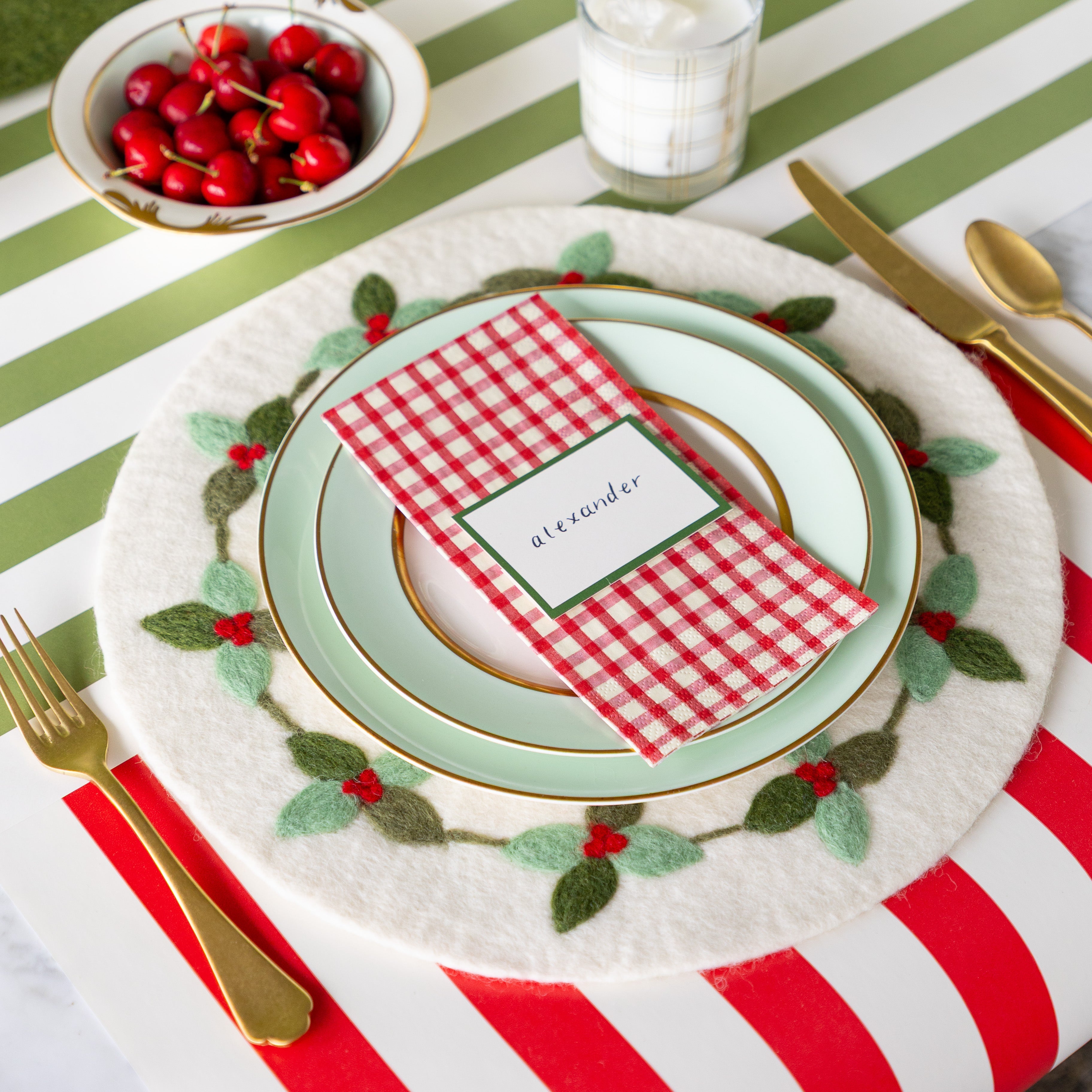 An elegant place setting featuring the Felt Mistletoe Berry Placemat, seafoam dinnerware with the Red Plaid Guest Napkin and Dark Green Frame Place Card atop, and gold flatware on the Red Classic Stripe and Moss Classic Stripe Runners.
