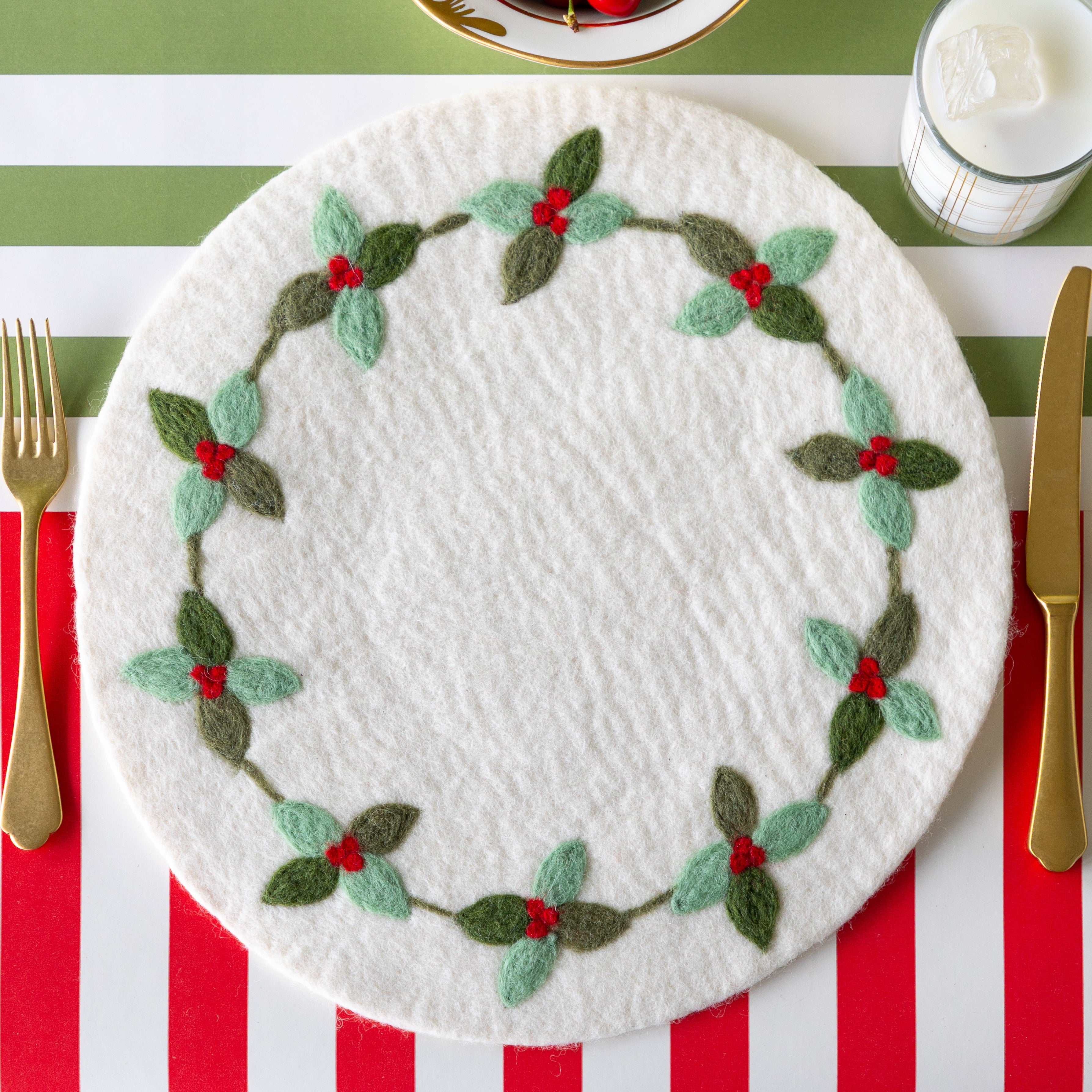 A place setting with no plates, featuring the Felt Berry Wreath Placemat, gold flatware and a glass of milk on the Red Classic Stripe and Moss Green Classic Stripe Runners.