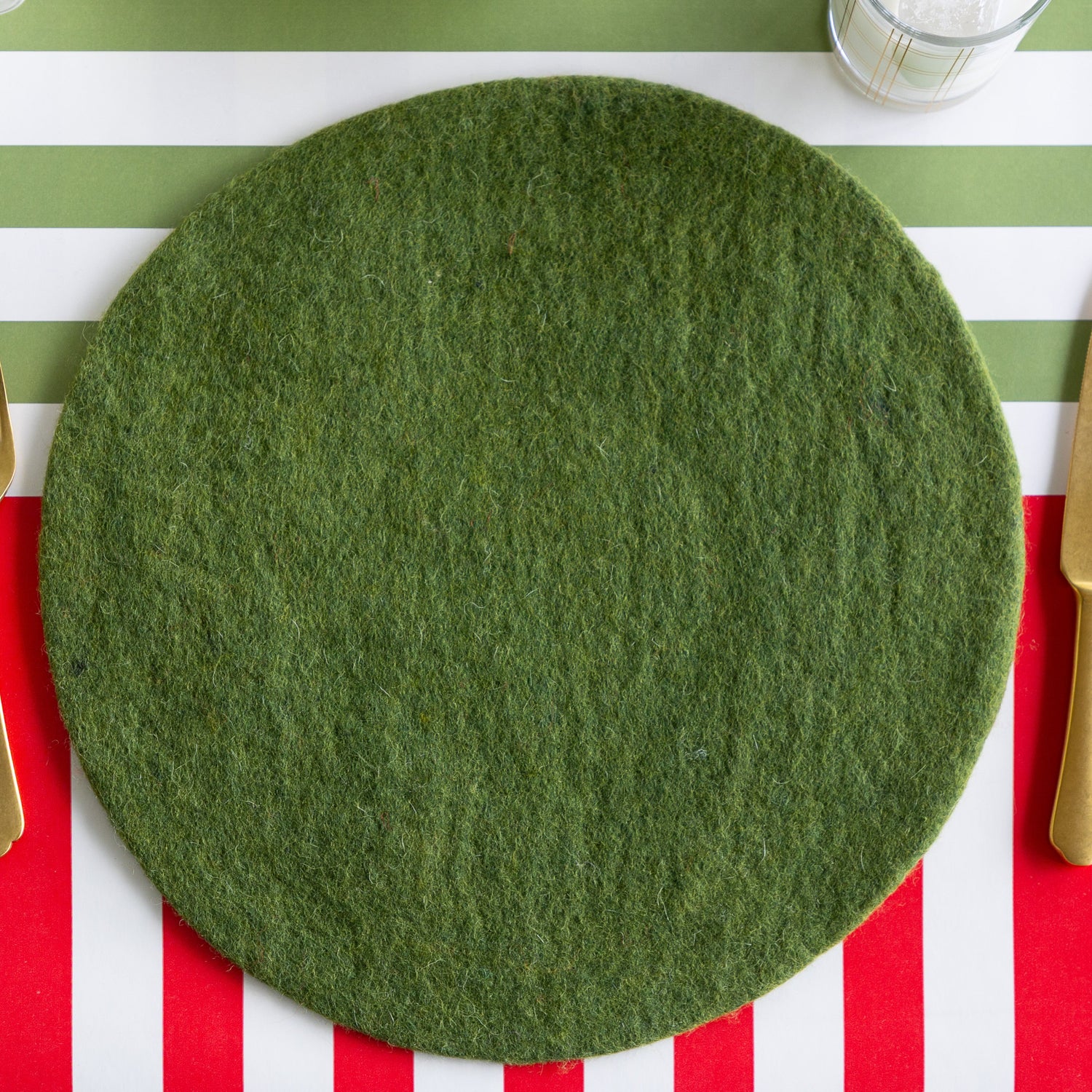A place setting featuring the Forest Green Felt Placemat and gold flatware on the Red Classic and Moss Classic Stripe Runners.