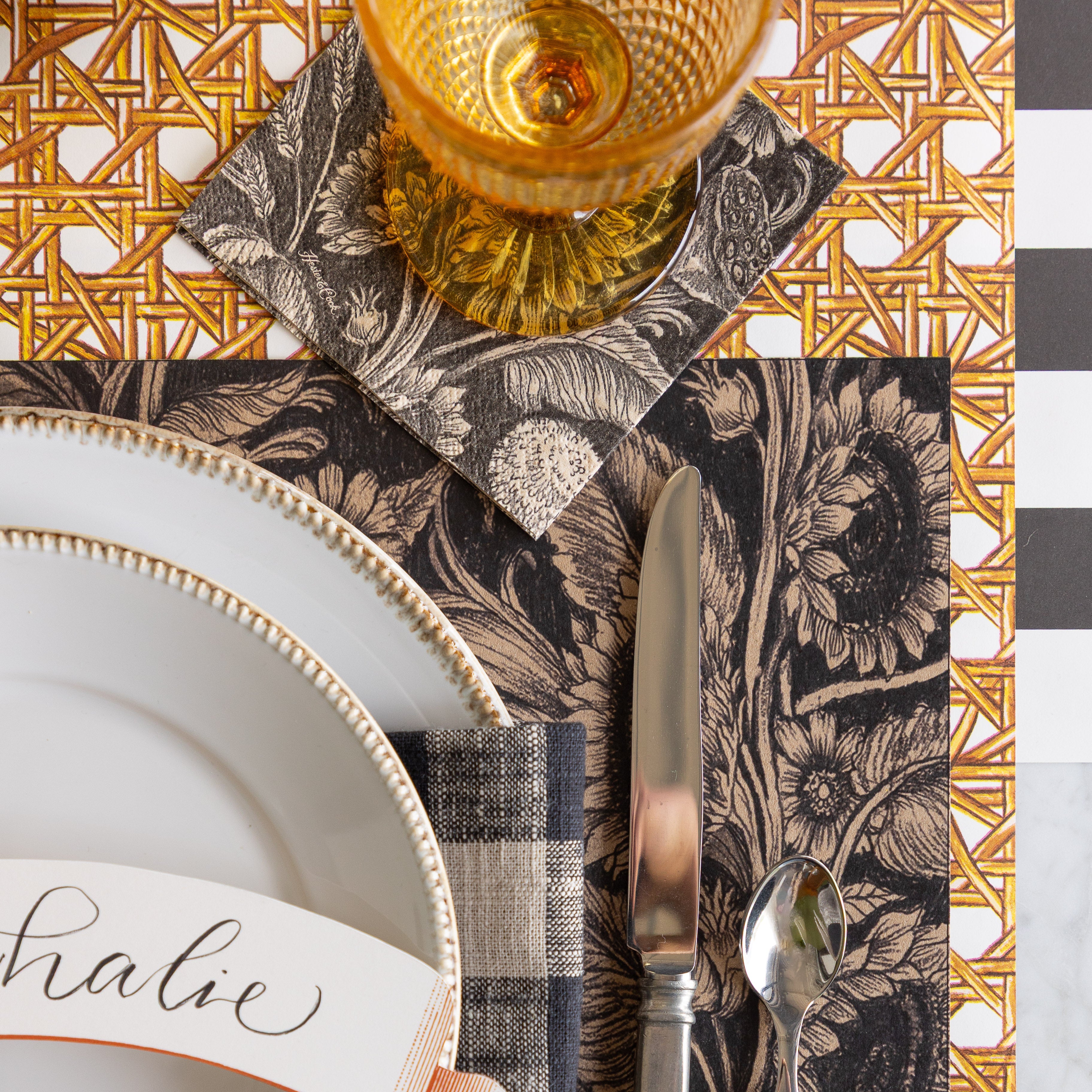A place setting with the Sunflower Field Placemat, Vintage Sunflower Cocktail Napkin under an empty glass, Rattan Weave Runner rolled out vertically and Black Classic Stripe Runner rolled out horizontally underneath.