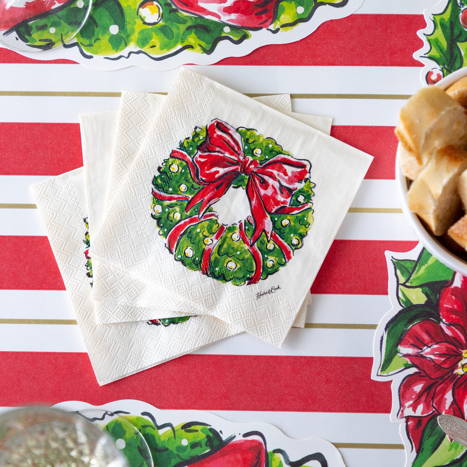 A fanned out stack of Holiday Wreath Cocktail Napkins on the Red & Gold Awning Stripe Runner.