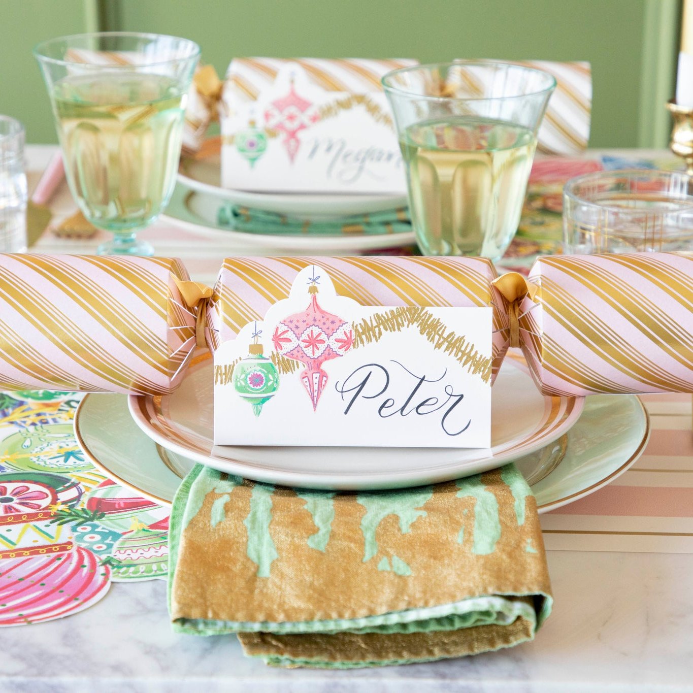 The Ornament Place Card in front of a festive cracker, resting on top of dinner plates with a marbled napkin in between.
