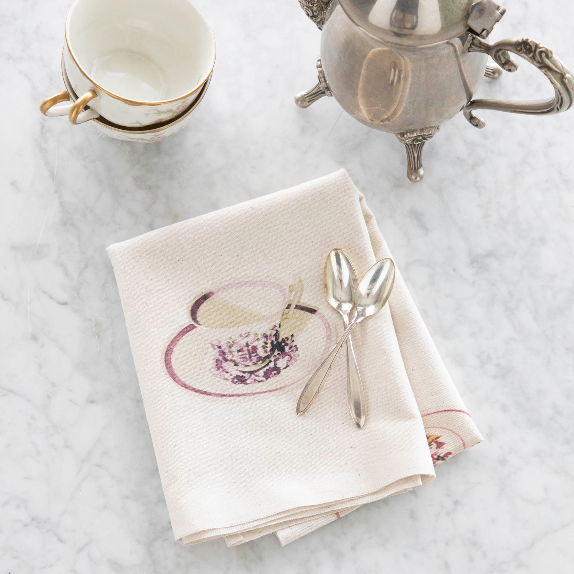 Close-up of the Tea Time Tea Towel folded and resting on a table, showing an illustrated teacup printed on the towel.