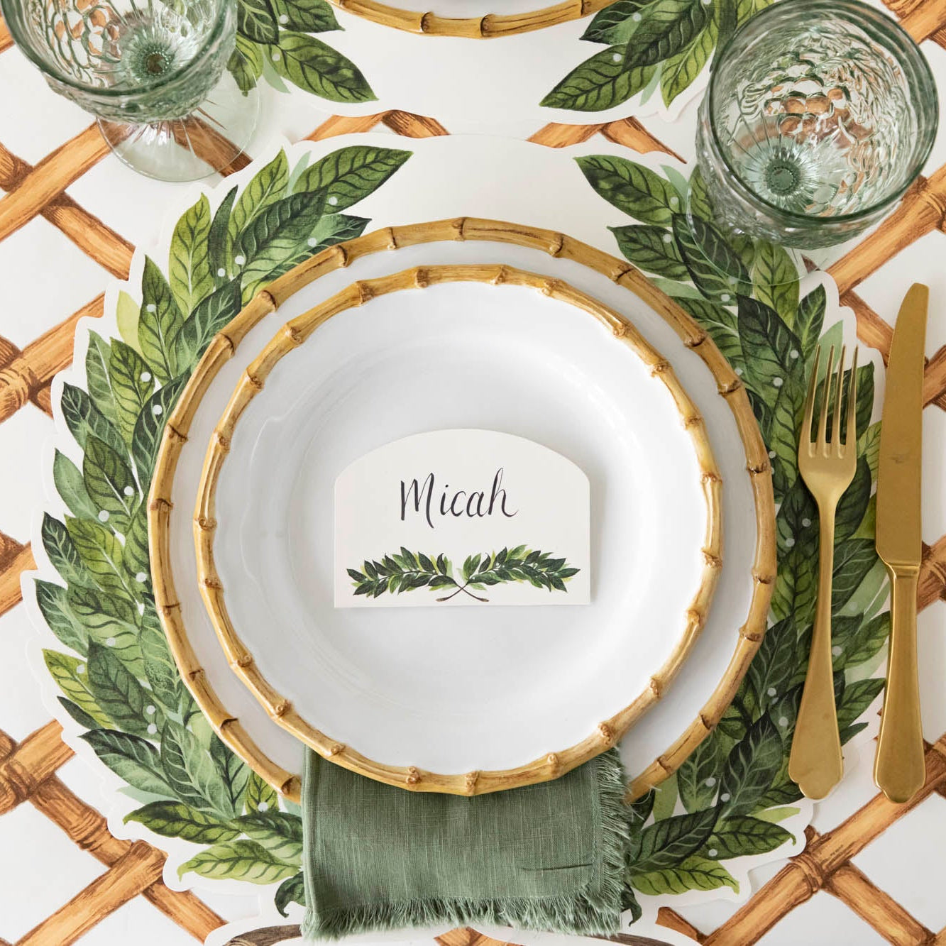 Table setting with the Die-cut Laurel Wreath Placemat, bamboo dinner plates with Laurel Place Card atop and gold flatware on the Bamboo Lattice Runner.