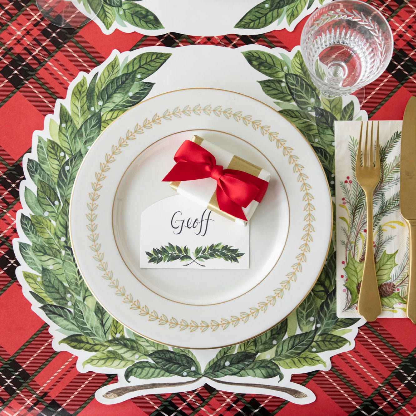 Christmas-themed table setting with the Die-cut Laurel Wreath Placemat, laurel design plate with a small present and Laurel Place Card atop on the Red Plaid Runner.