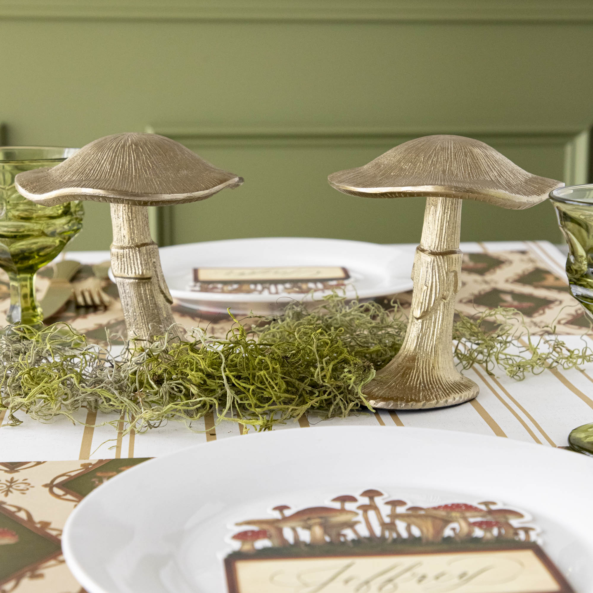 A gold metal mushroom figurine placed on a table with a harvest tablescape in the background.