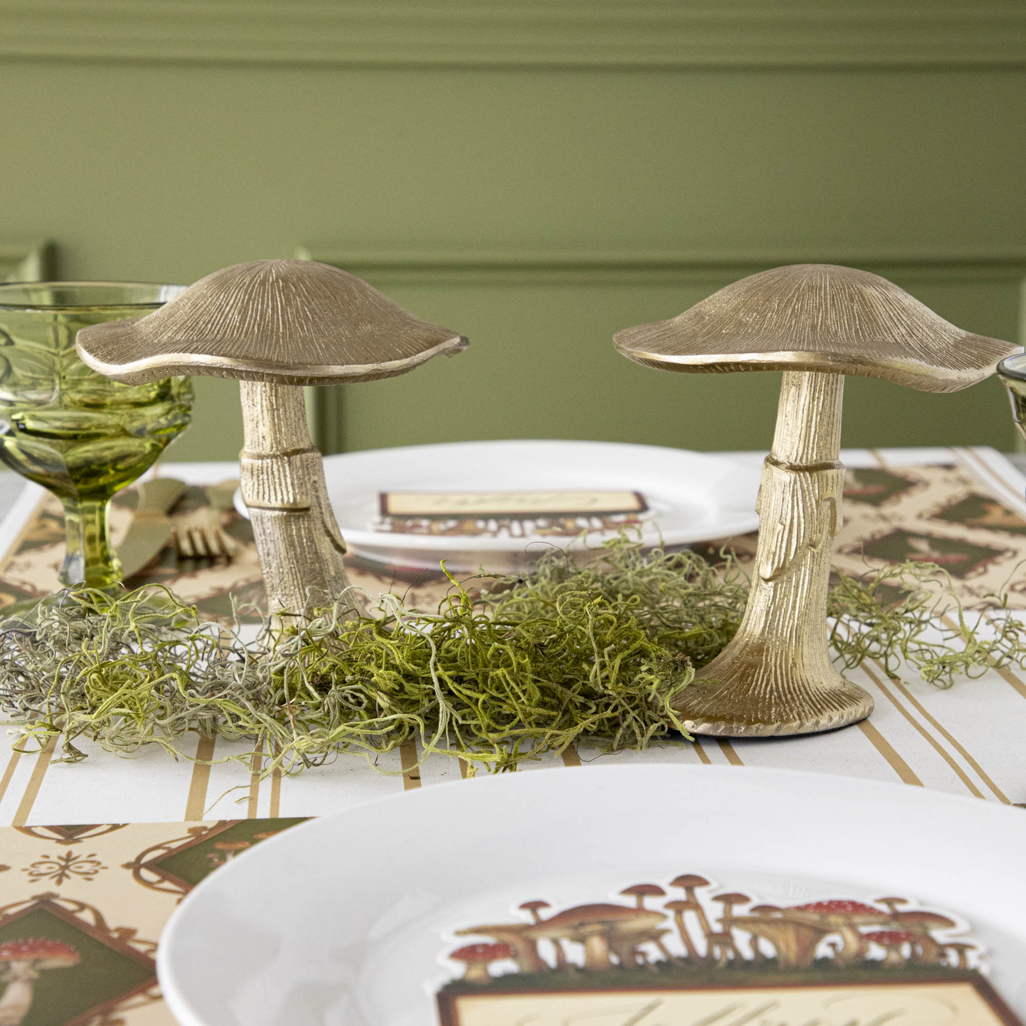 A gold metal mushroom figurine placed on a table with a harvest tablescape in the background.
