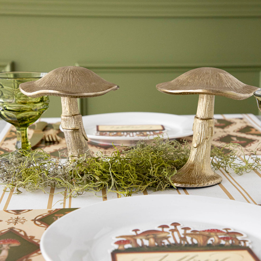 A gold metal mushroom figurine placed on a table with a harvest tablescape in the background.