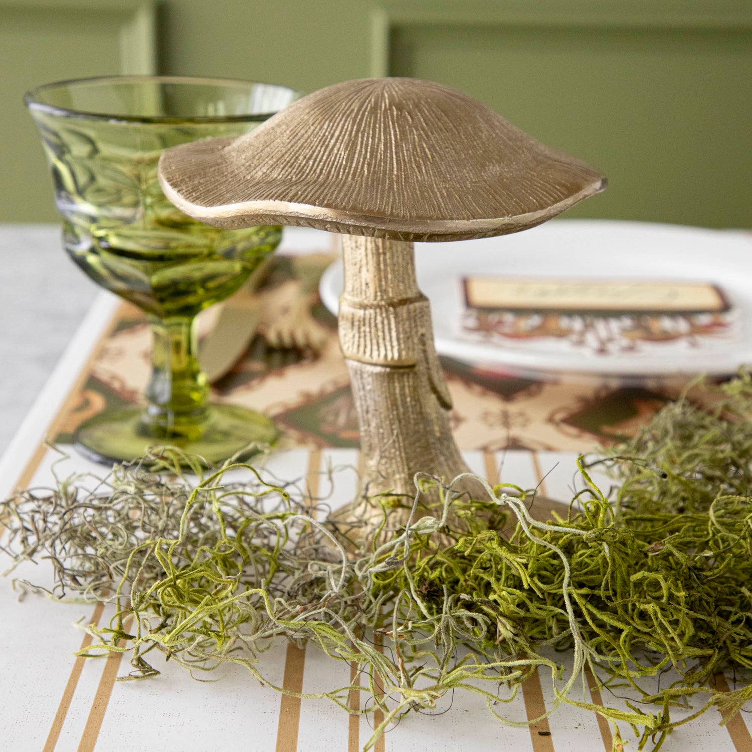 A gold metal mushroom figurine placed on a table with a harvest tablescape in the background.