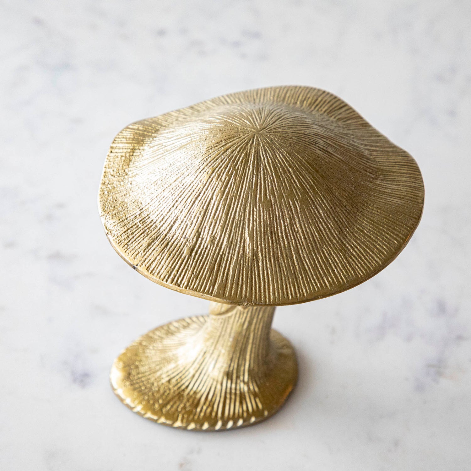 A gold metal mushroom figurine placed on a white marble table.