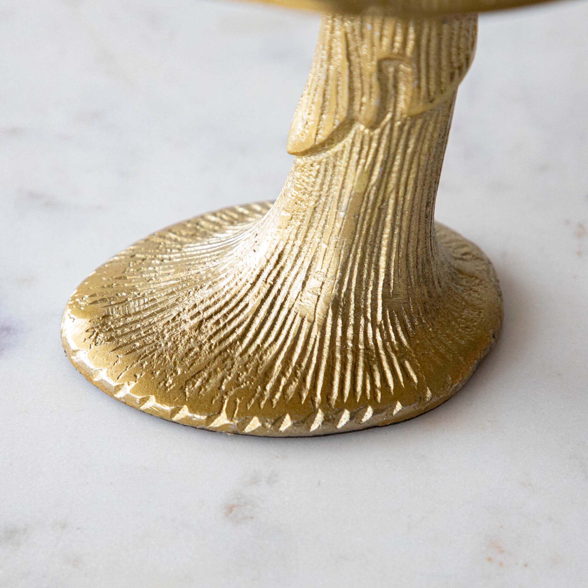 Detail shot of a gold metal mushroom figurine placed on a white marble table.