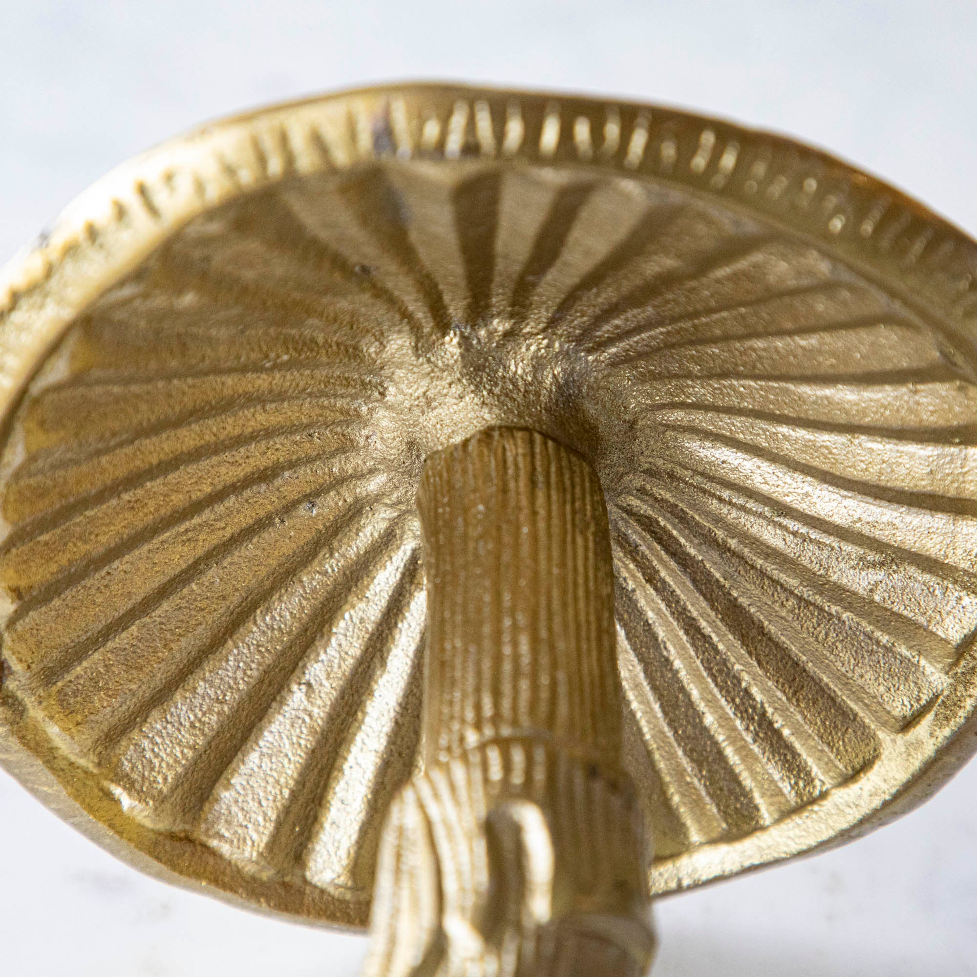 Detail shot of the gold metal mushroom figurine placed on a white marble table.