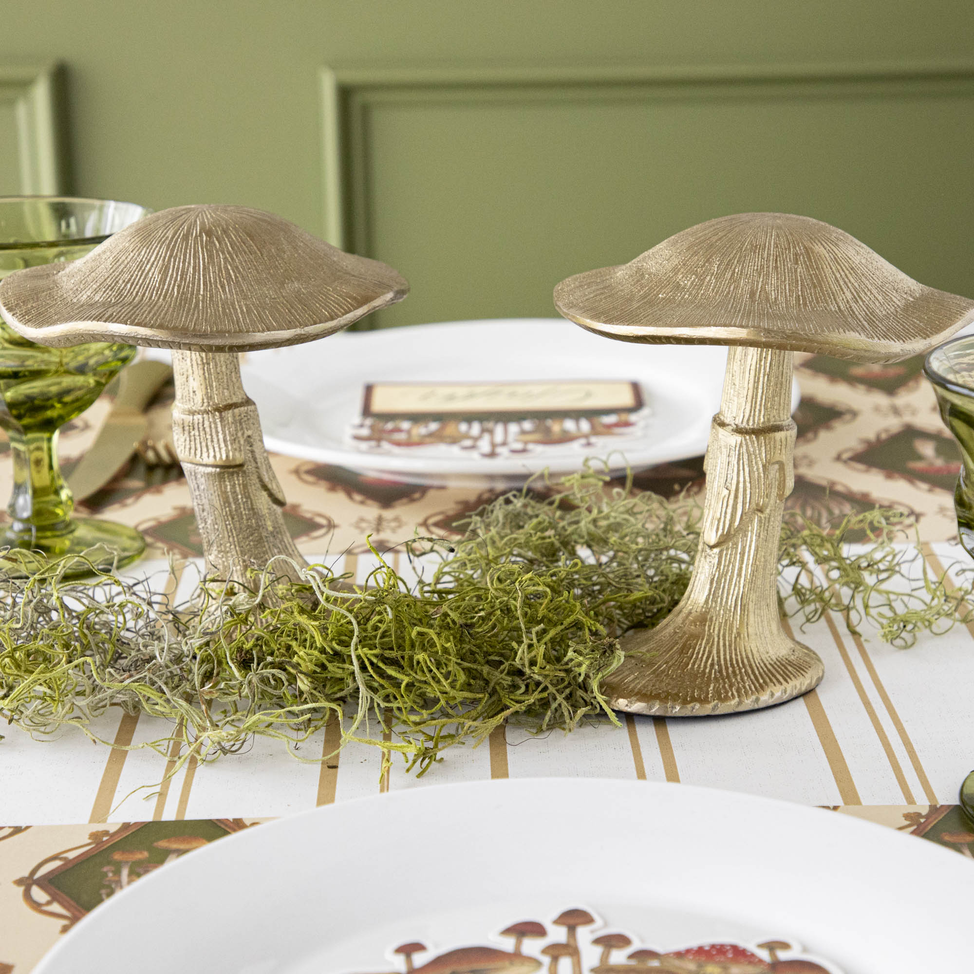 A gold metal mushroom figurine placed on a table with a harvest tablescape in the background.