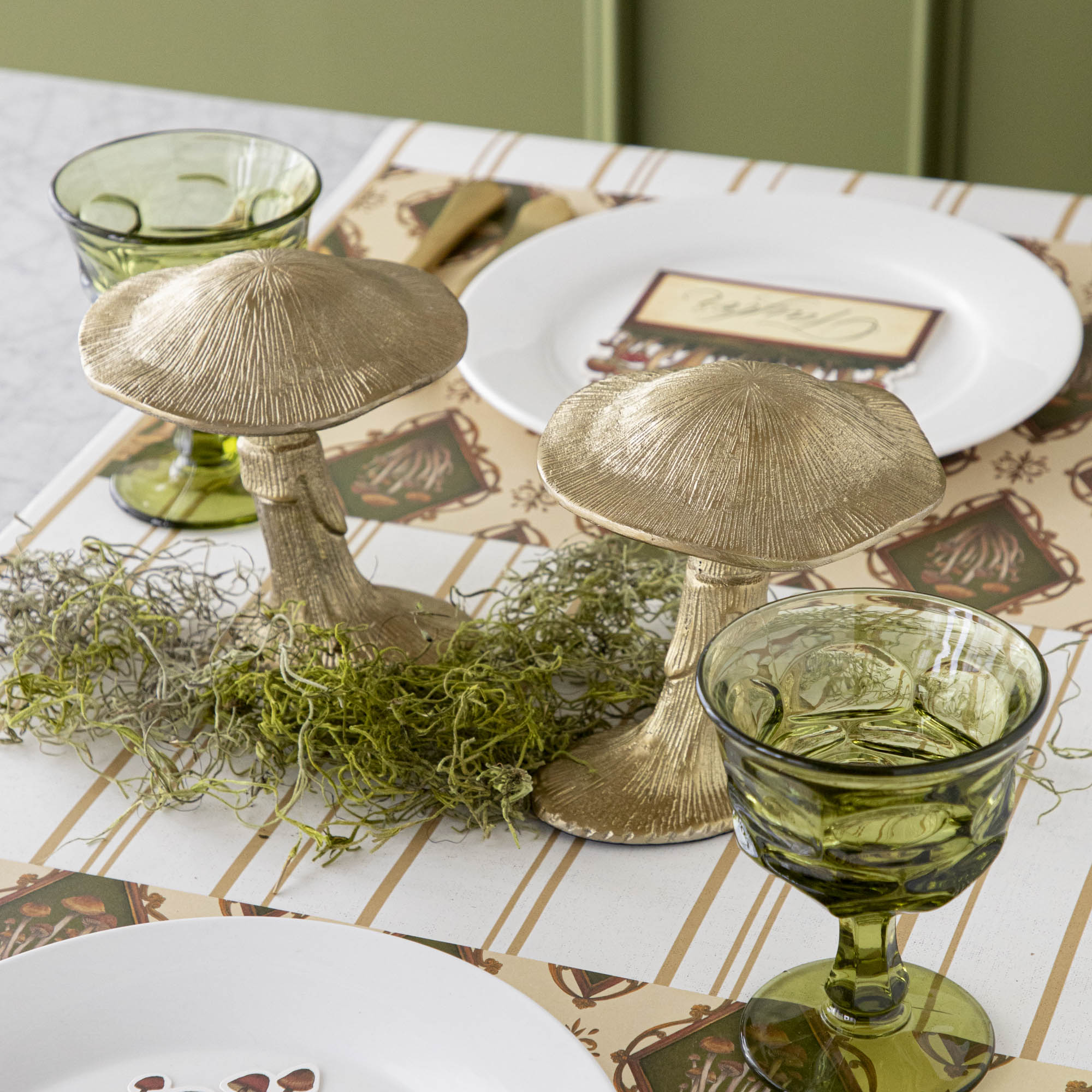 A gold metal mushroom figurine placed on a table with a harvest tablescape in the background.