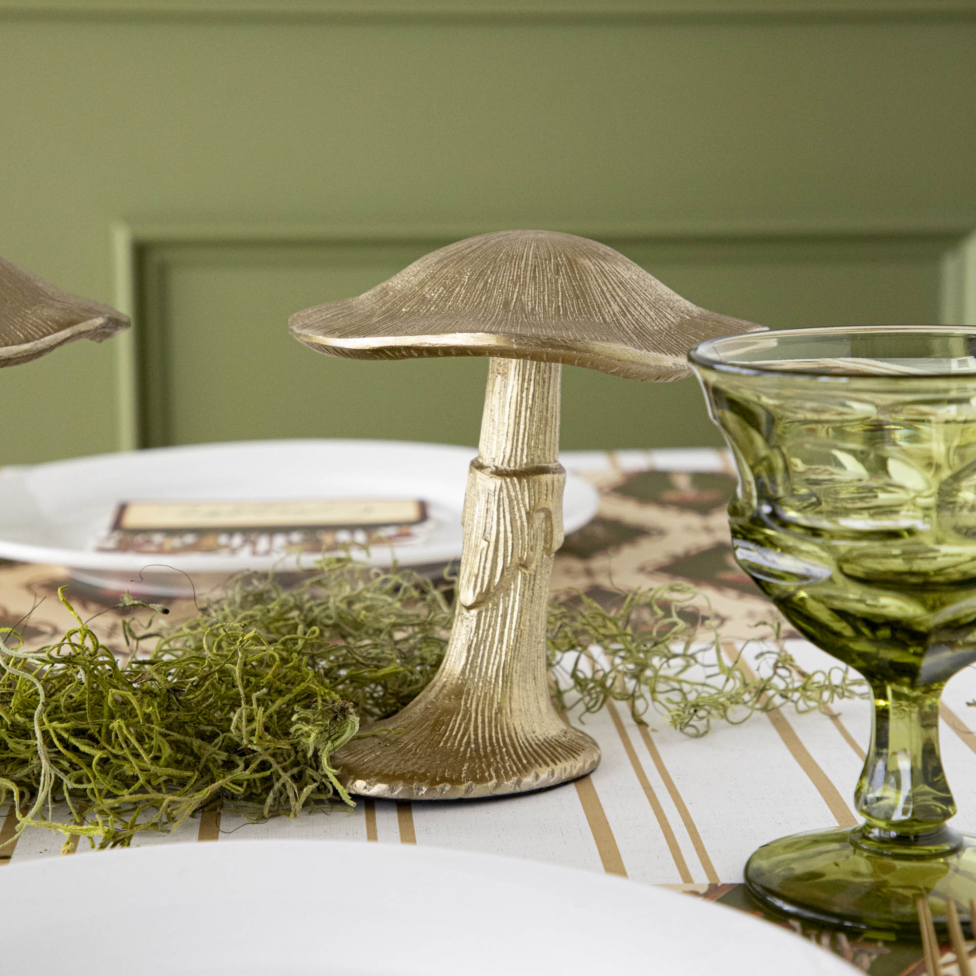 A gold metal mushroom figurine placed on a table with a harvest tablescape in the background.