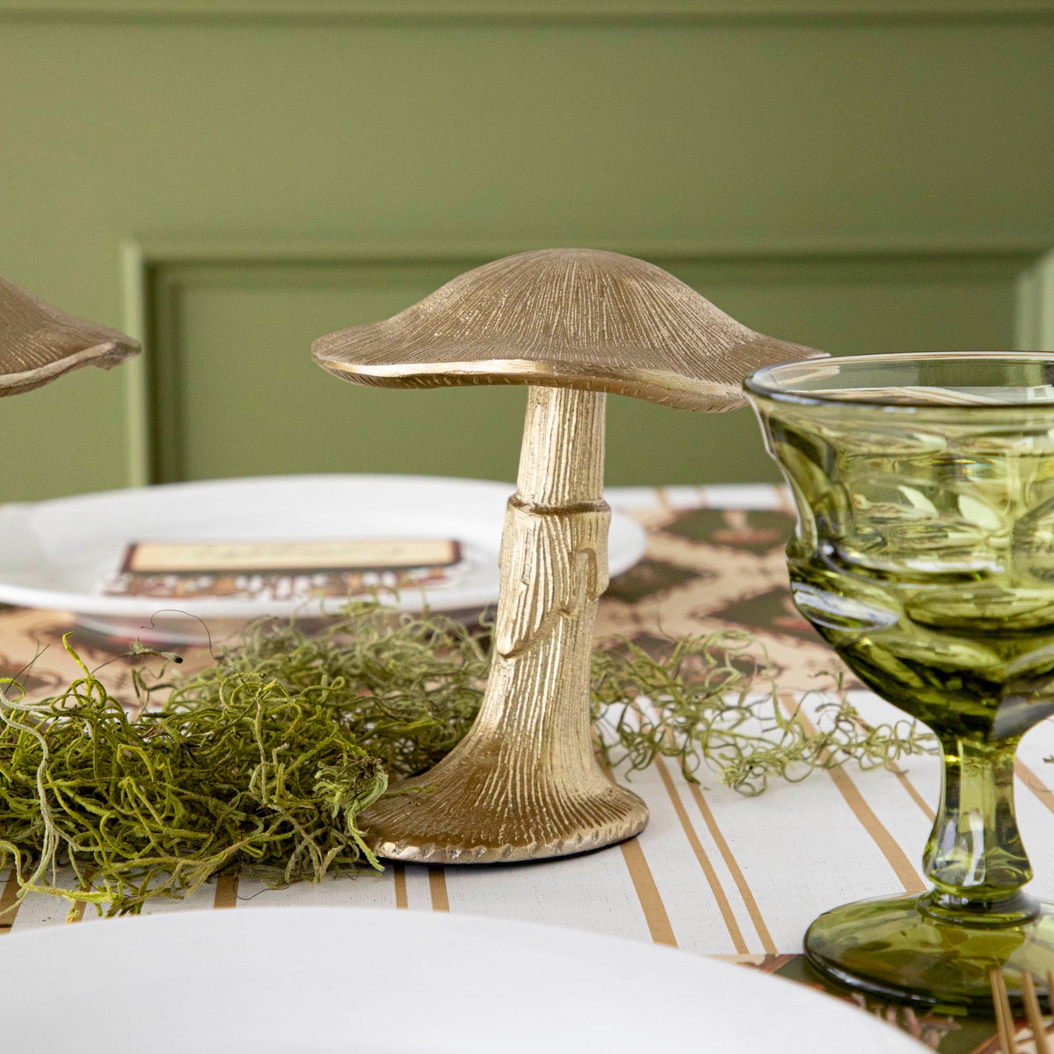 A gold metal mushroom figurine placed on a table with a harvest tablescape in the background.