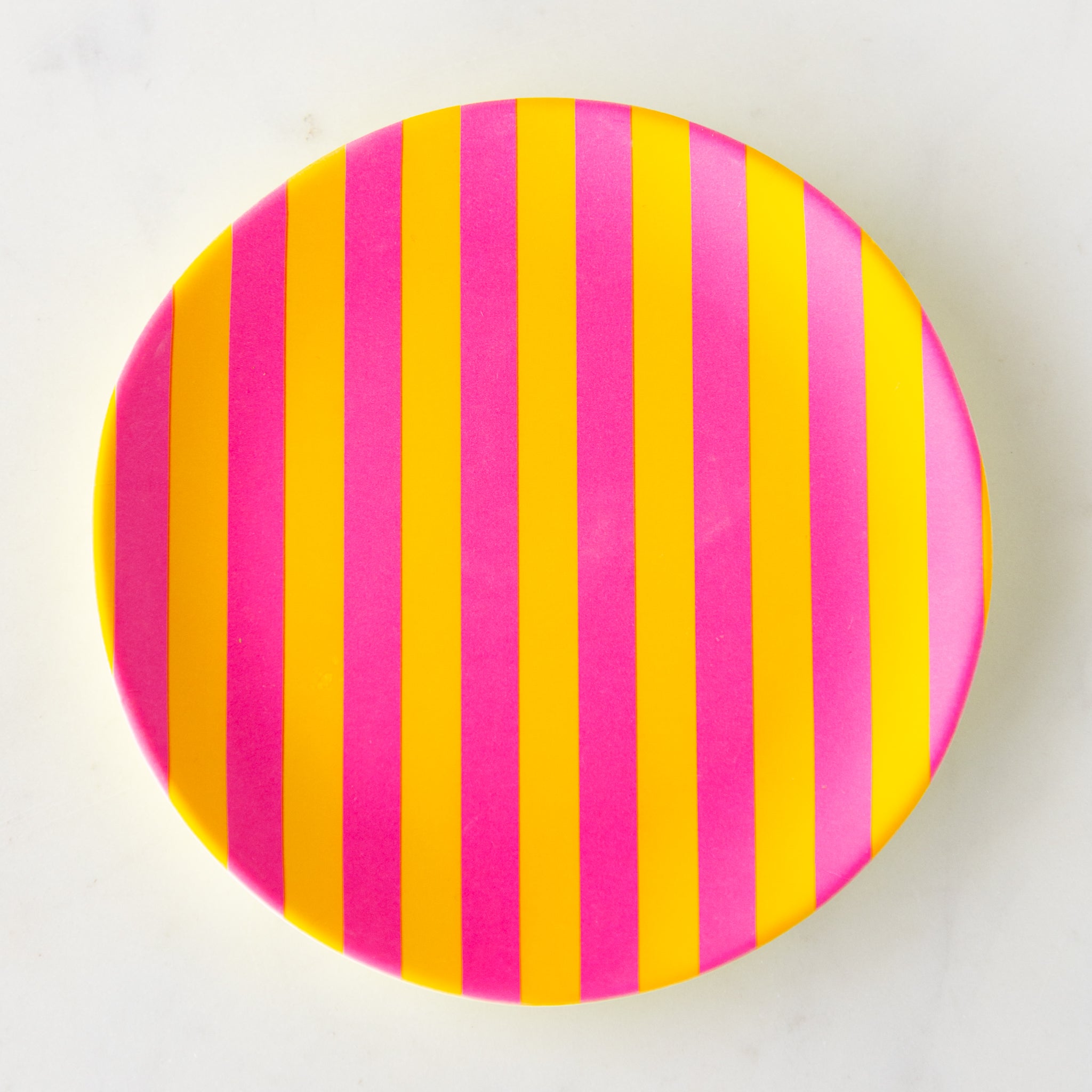 A round Stripe Melamine Plate with alternating vertical hot pink and yellow stripes on a marble table.