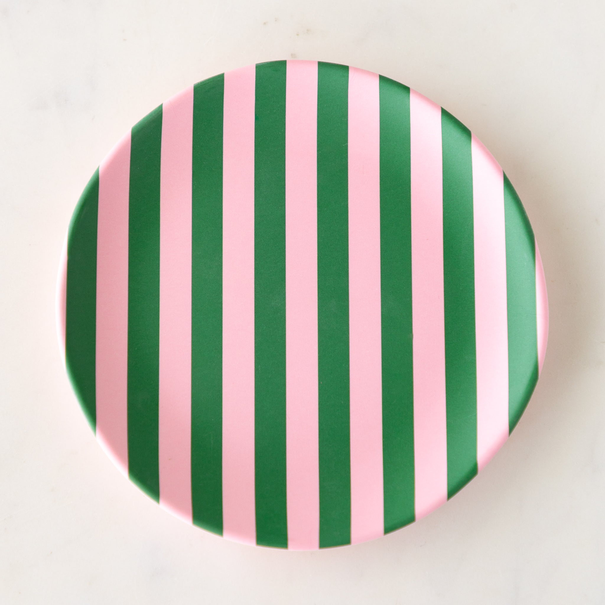 A round Stripe Melamine Plate with alternating vertical pink and green stripes on a marble table.