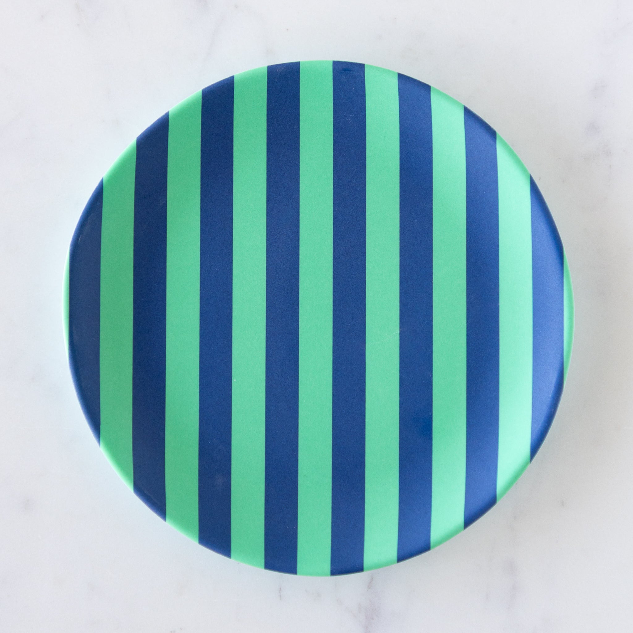 A round Stripe Melamine Plate with alternating vertical mint and navy stripes on a marble table.