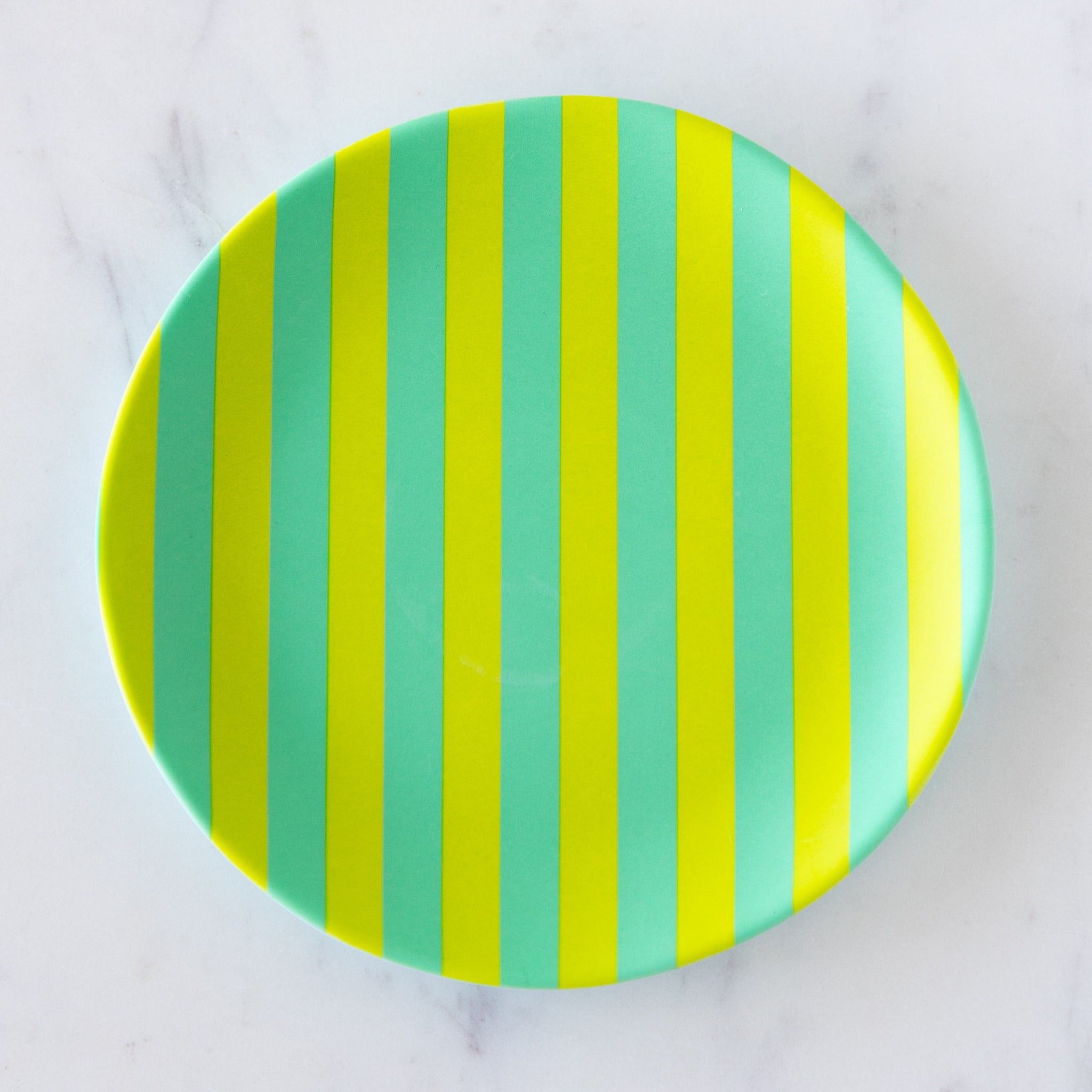 A round Stripe Melamine Plate with alternating vertical lime green and teal stripes on a marble table.