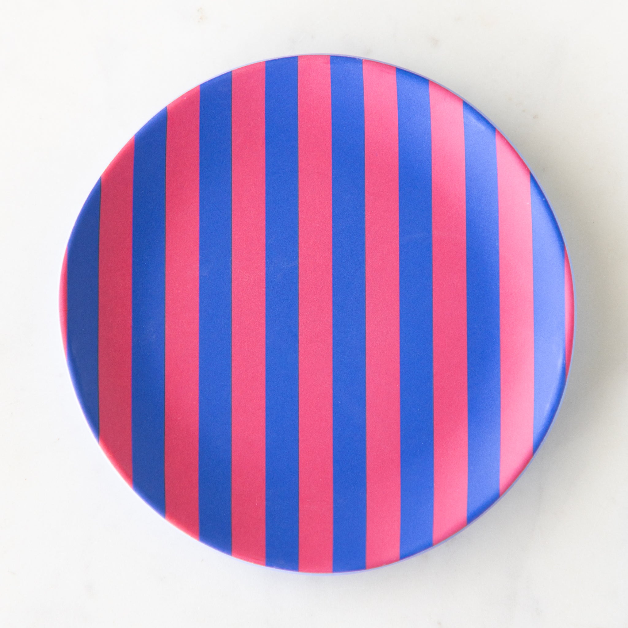 A round Stripe Melamine Plate with alternating vertical pink and blue stripes on a marble table.