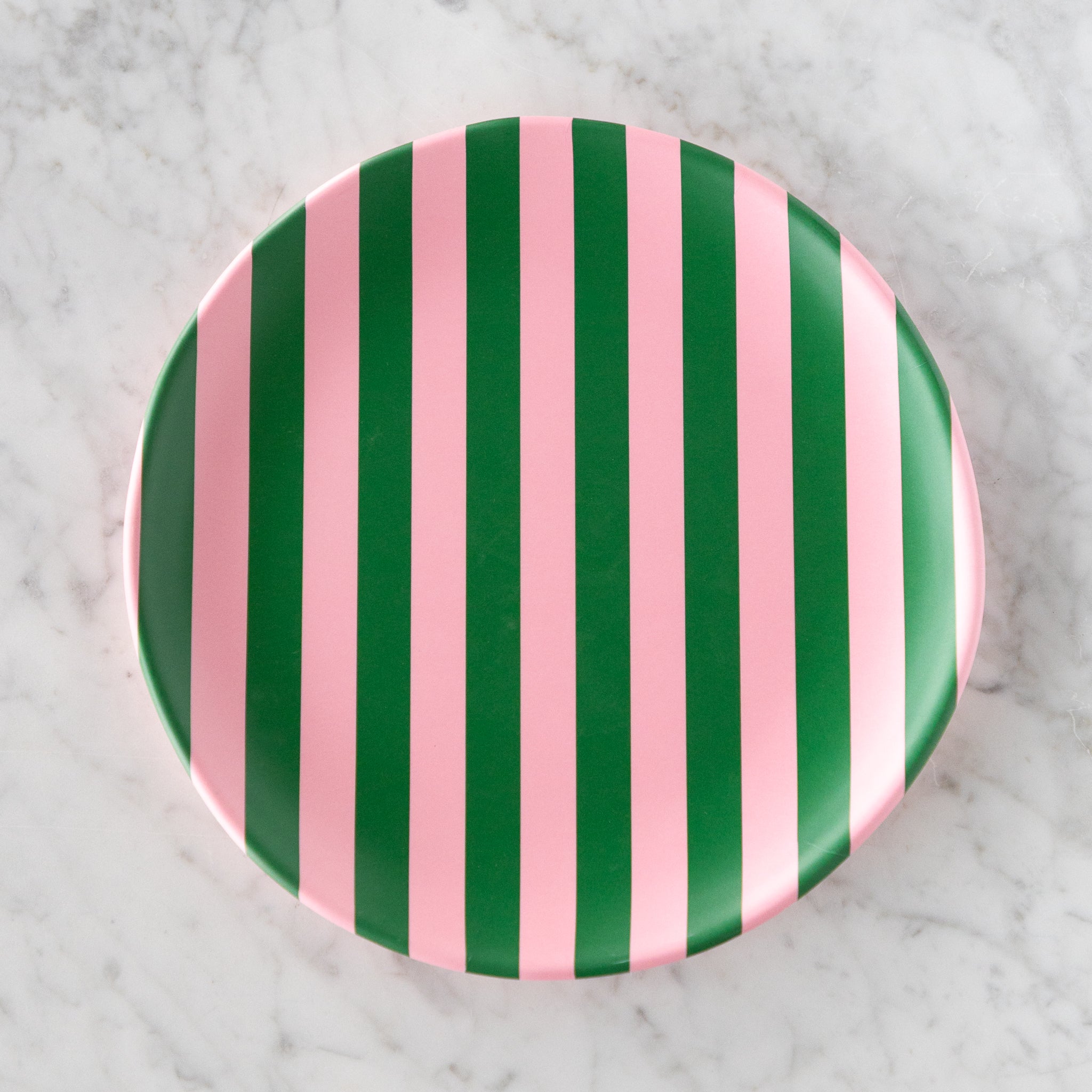 A round Stripe Melamine Plate with alternating vertical pink and green stripes on a marble table.