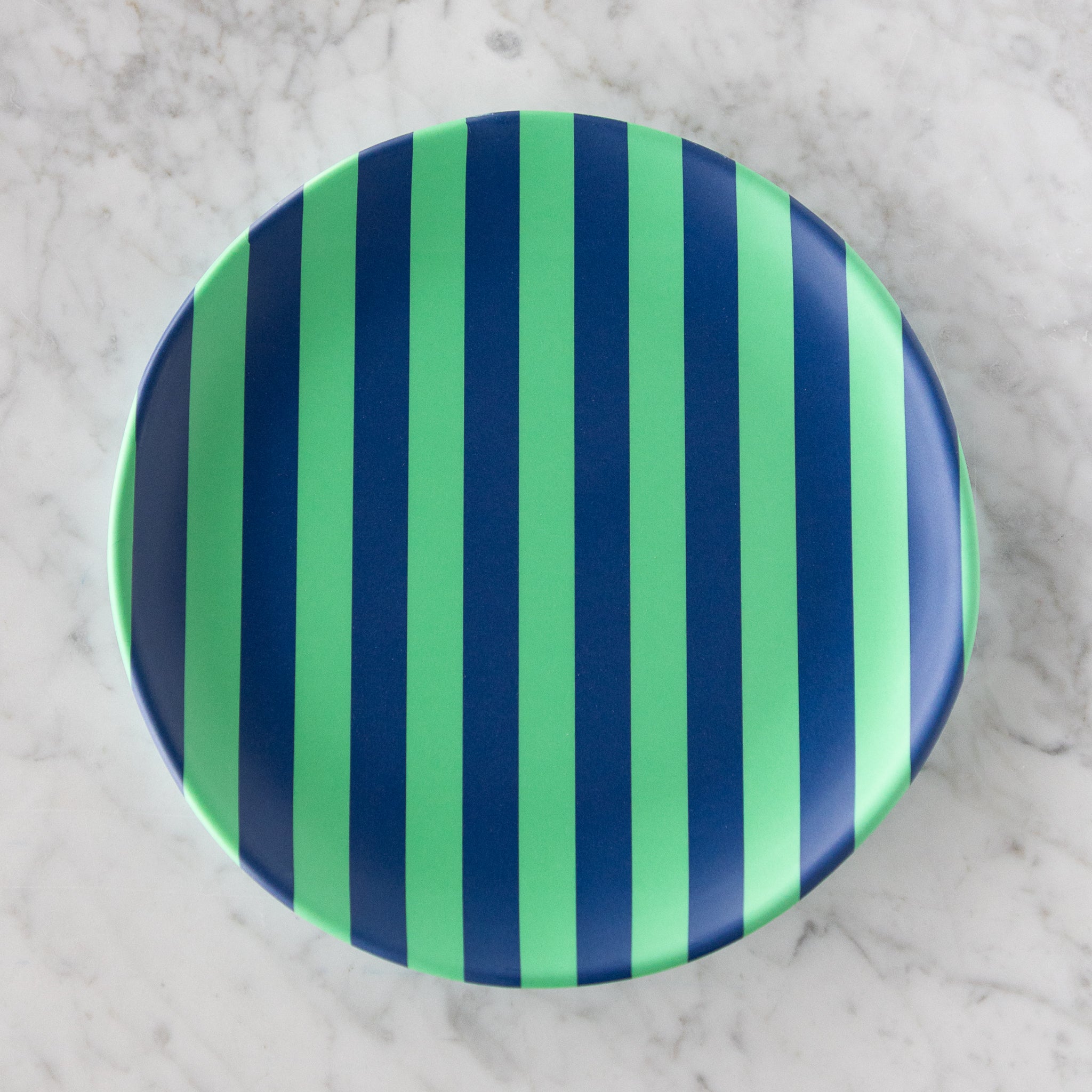 A round Stripe Melamine Plate with alternating vertical mint and navy stripes on a marble table.