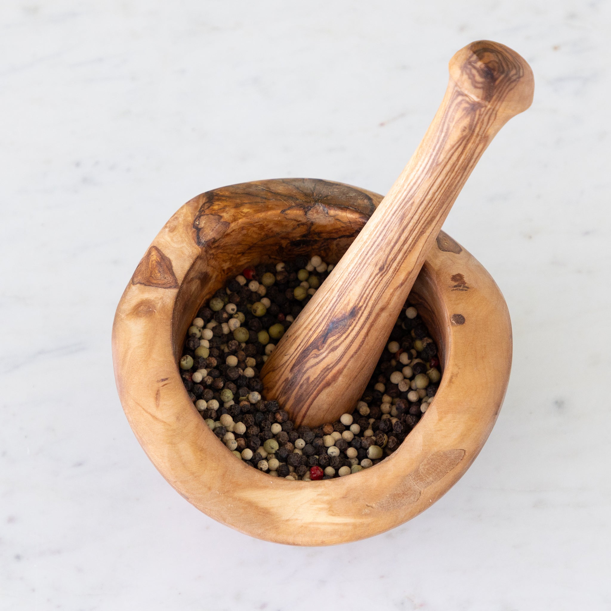 Wooden mortar and pestle with peppercorns on a light background.