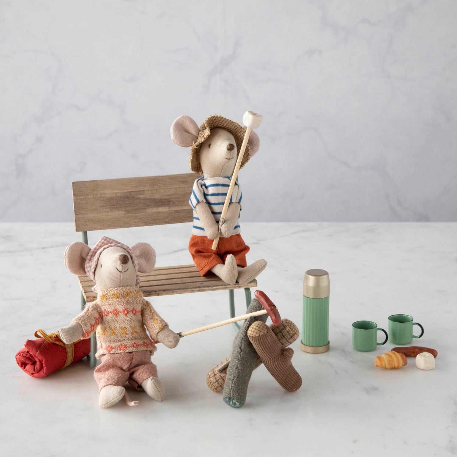 Two Maileg Mini Thermos and Cups Sets sitting on a bench.