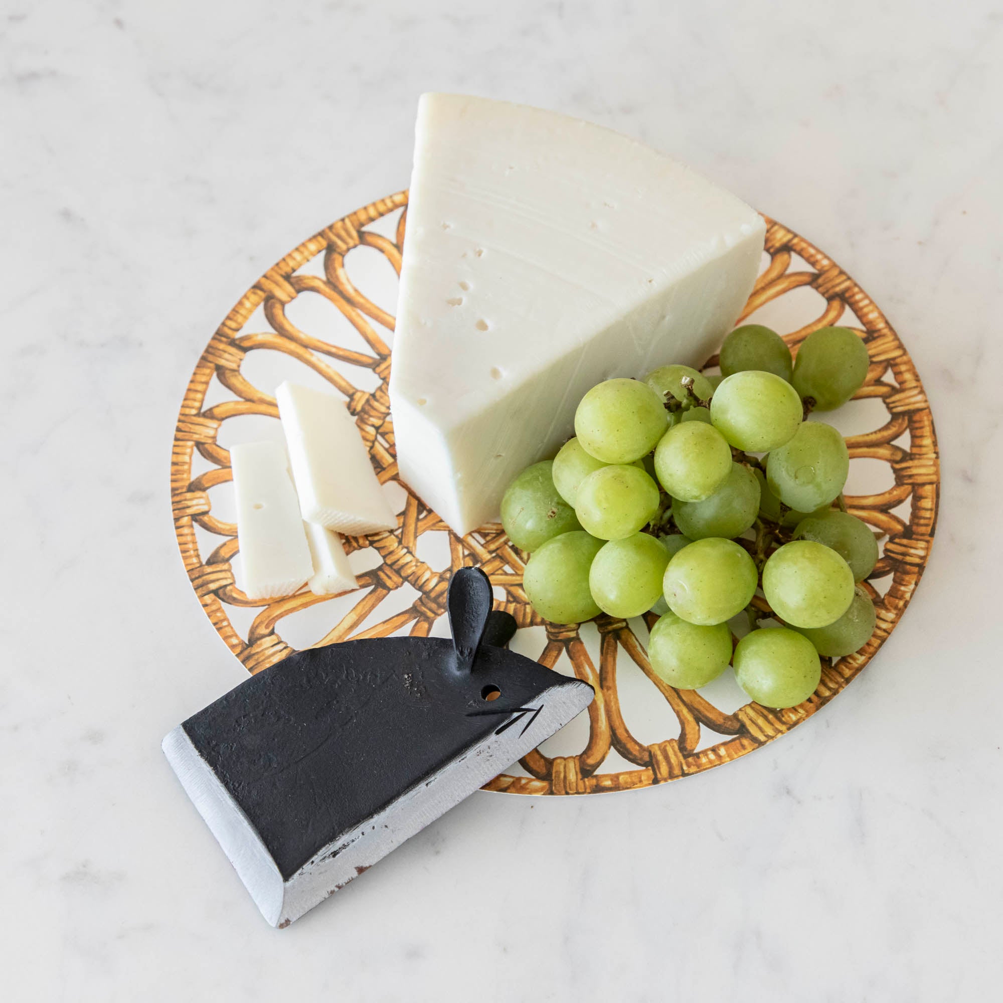Cheese and grapes on a plate with a cheese knife shaped like a mouse on a marble surface.