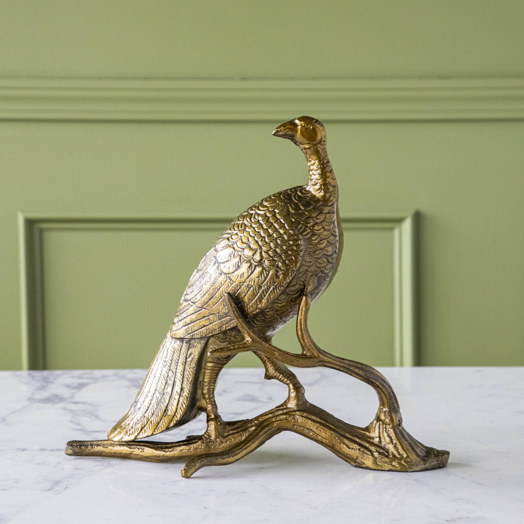 A bronze metal turkey on a branch decoration, placed on a dining table with green wall in the background.