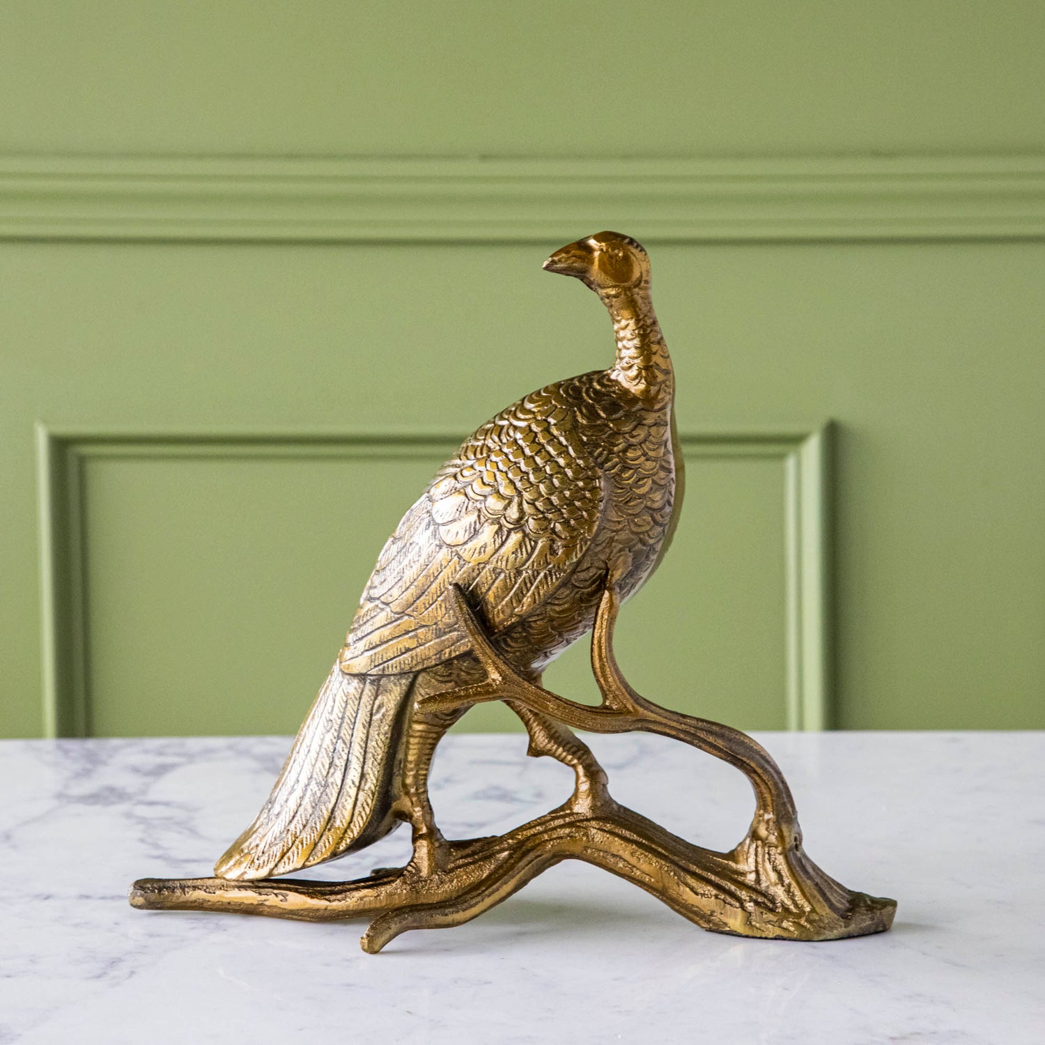 A bronze metal turkey on a branch decoration, placed on a dining table with green wall in the background.