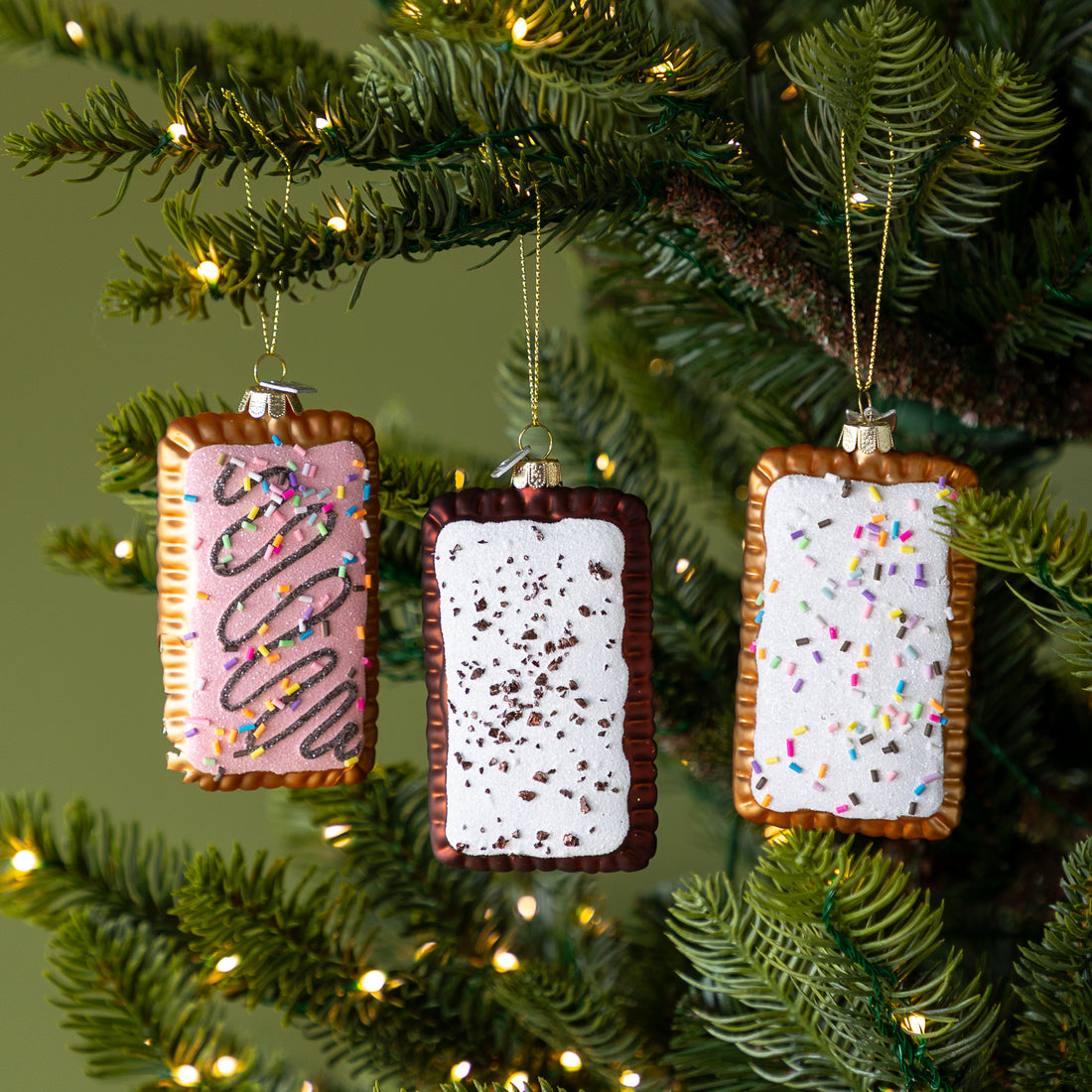Three Toaster Pastry Ornaments hanging on a lit Christmas tree.
