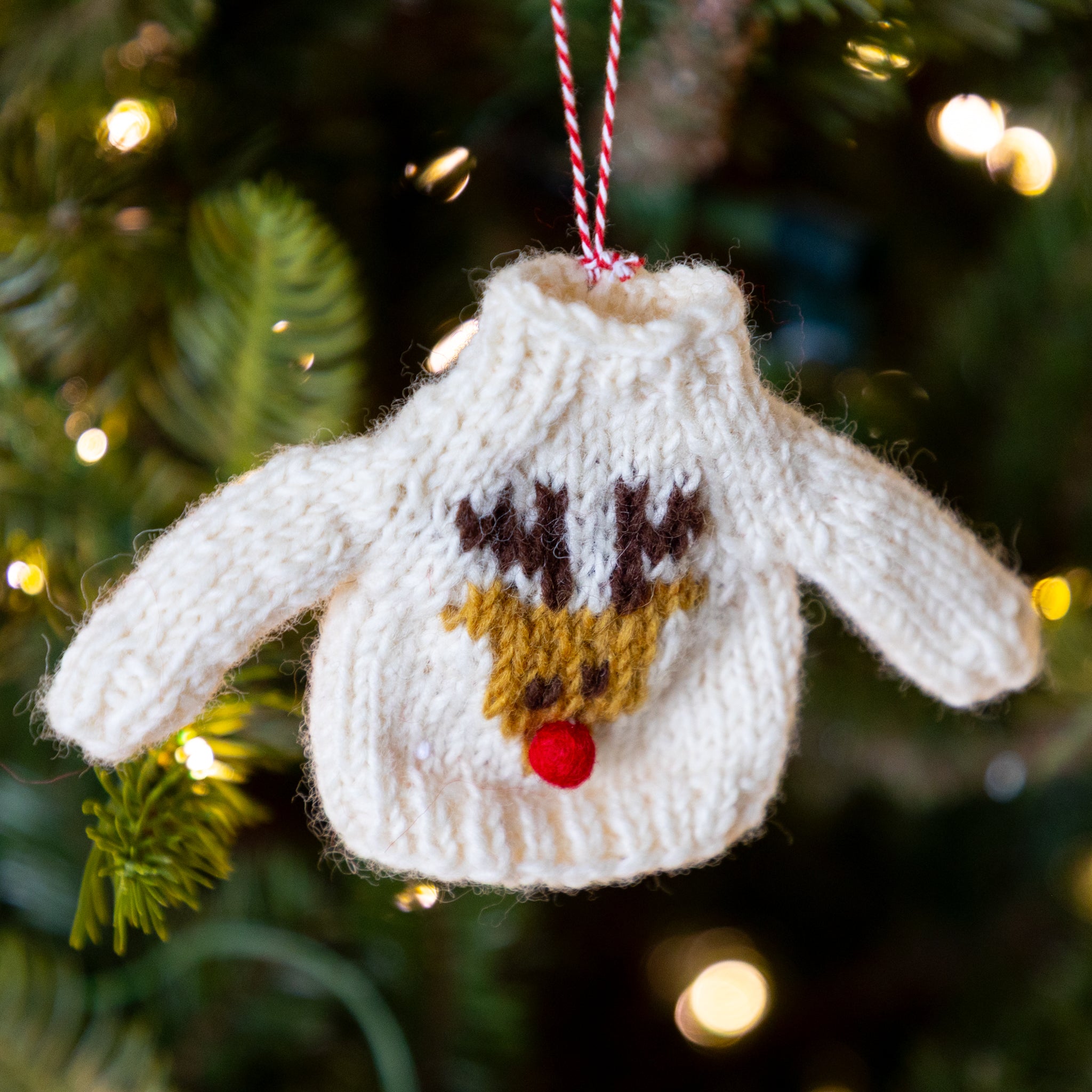 Knitted sweater ornament with a deer face design hanging on a Christmas tree.