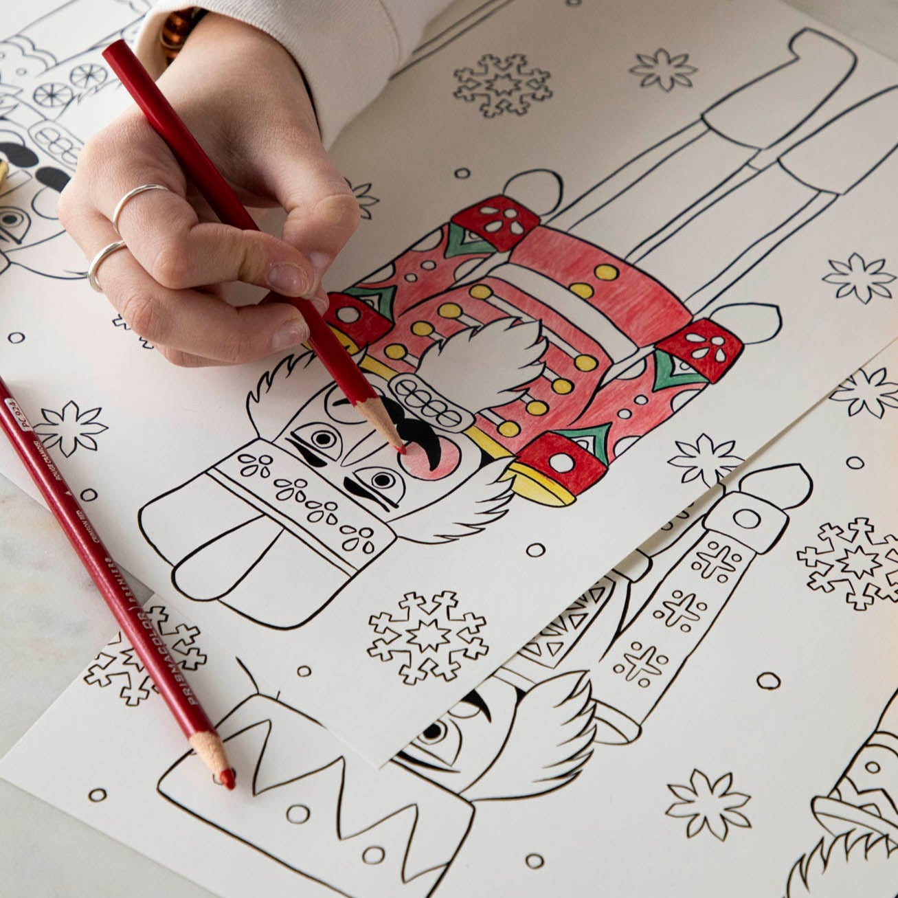 A woman coloring a nutcracker on the Christmas Coloring Placemat with scattered colored pencils.