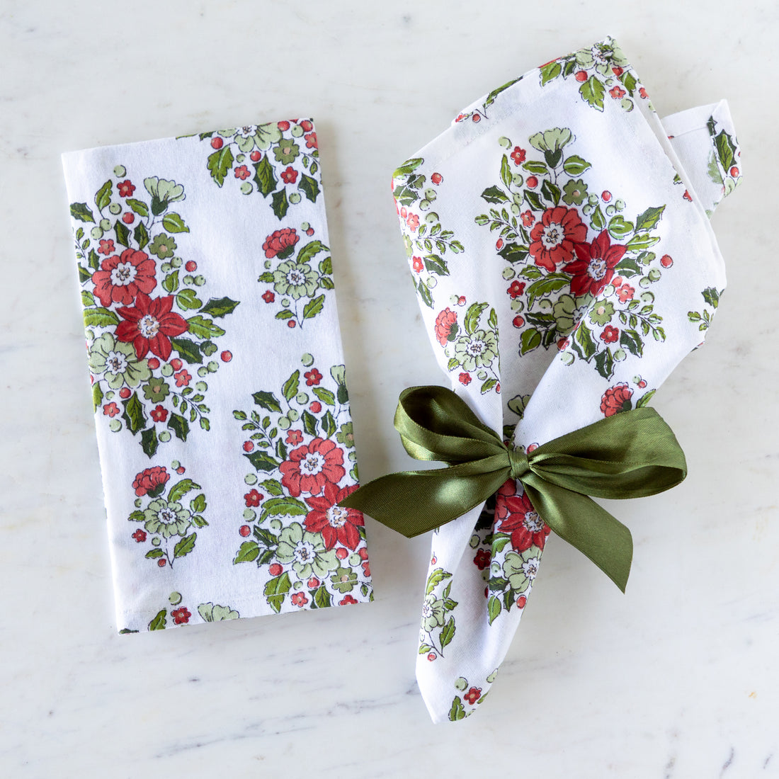 Holly &amp; Berry Ivory Napkins, one tied with Moss Green Fancy Ribbon and the other folded on a marble table.