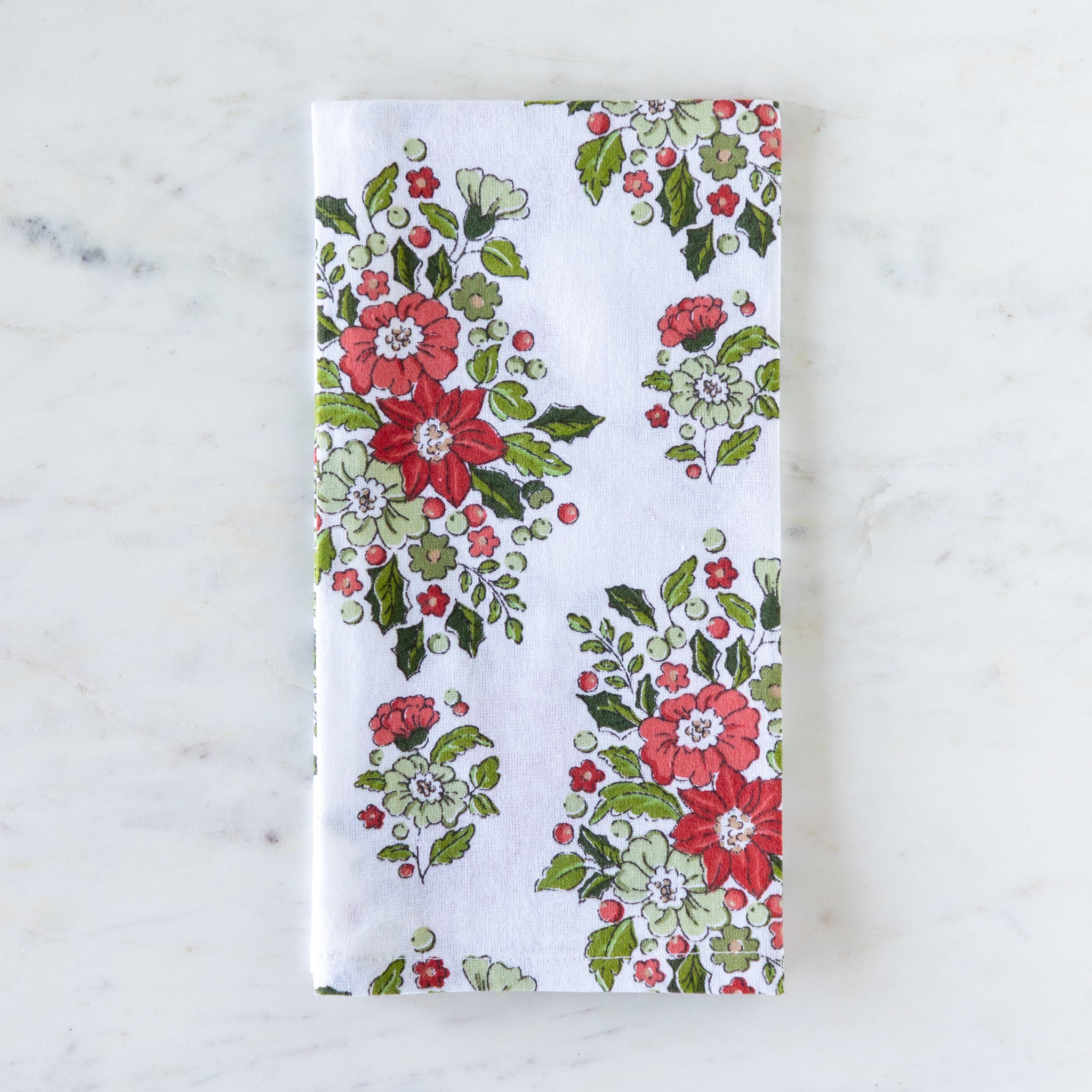 Holly & Berry Ivory Napkin folded on a marble table.