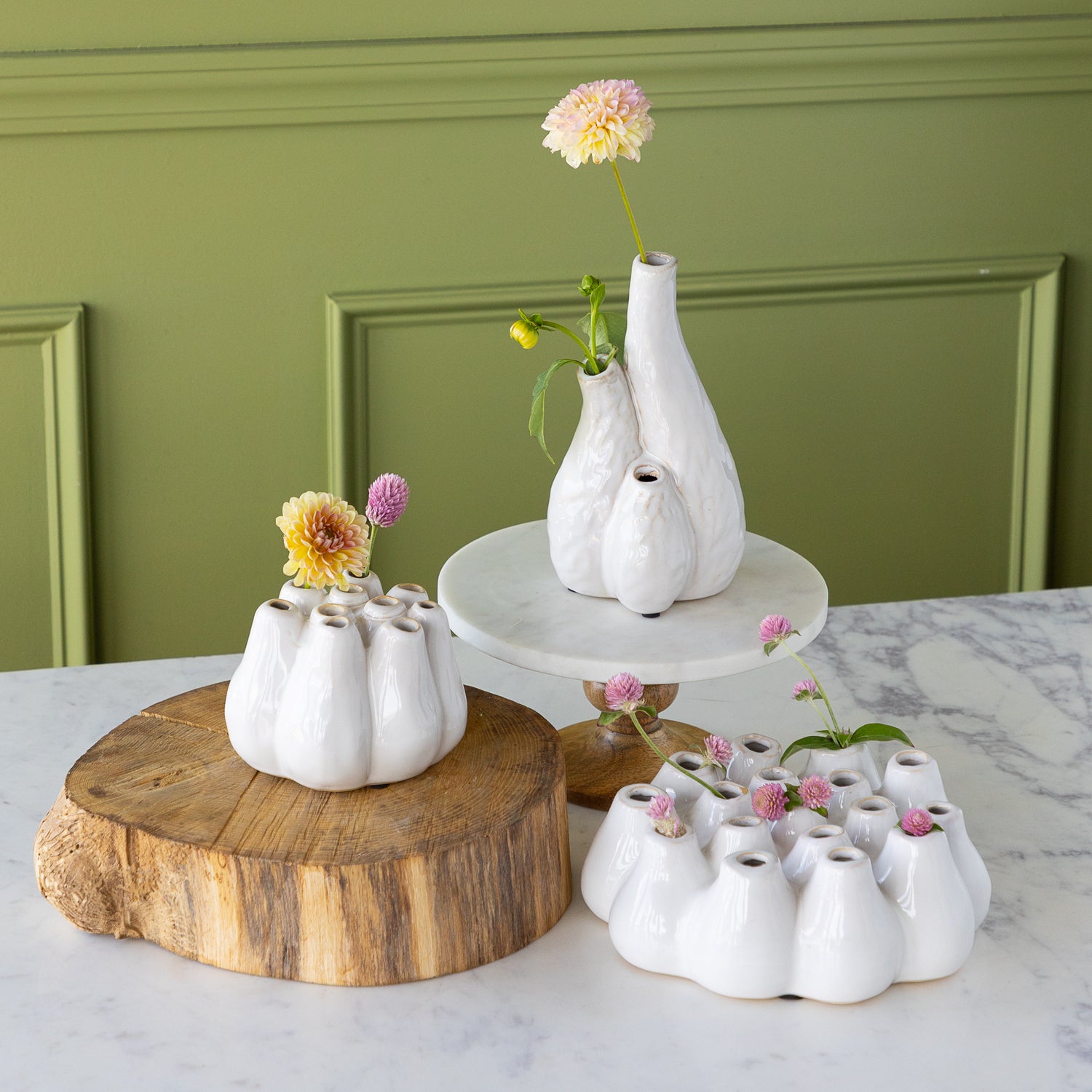White ceramic vases with flowers on a marble surface against a green wall.