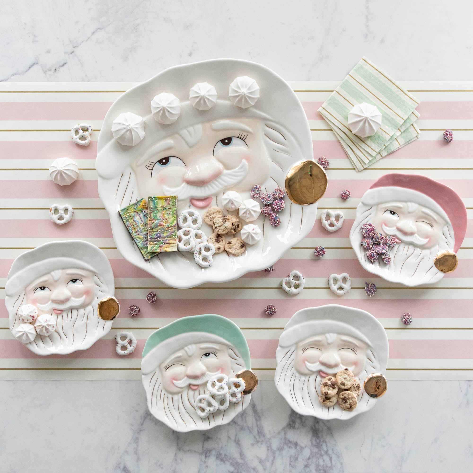 Papa Noel Cookie Plates with assorted treats, next to the Papa Noel Cookie Platter on the Pink & Gold Awning Stripe Runner.