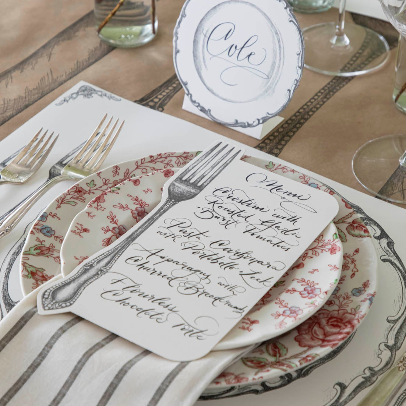 Vintage Fork Table Card with a menu written on it, resting on dinner plates on a table setting for one.