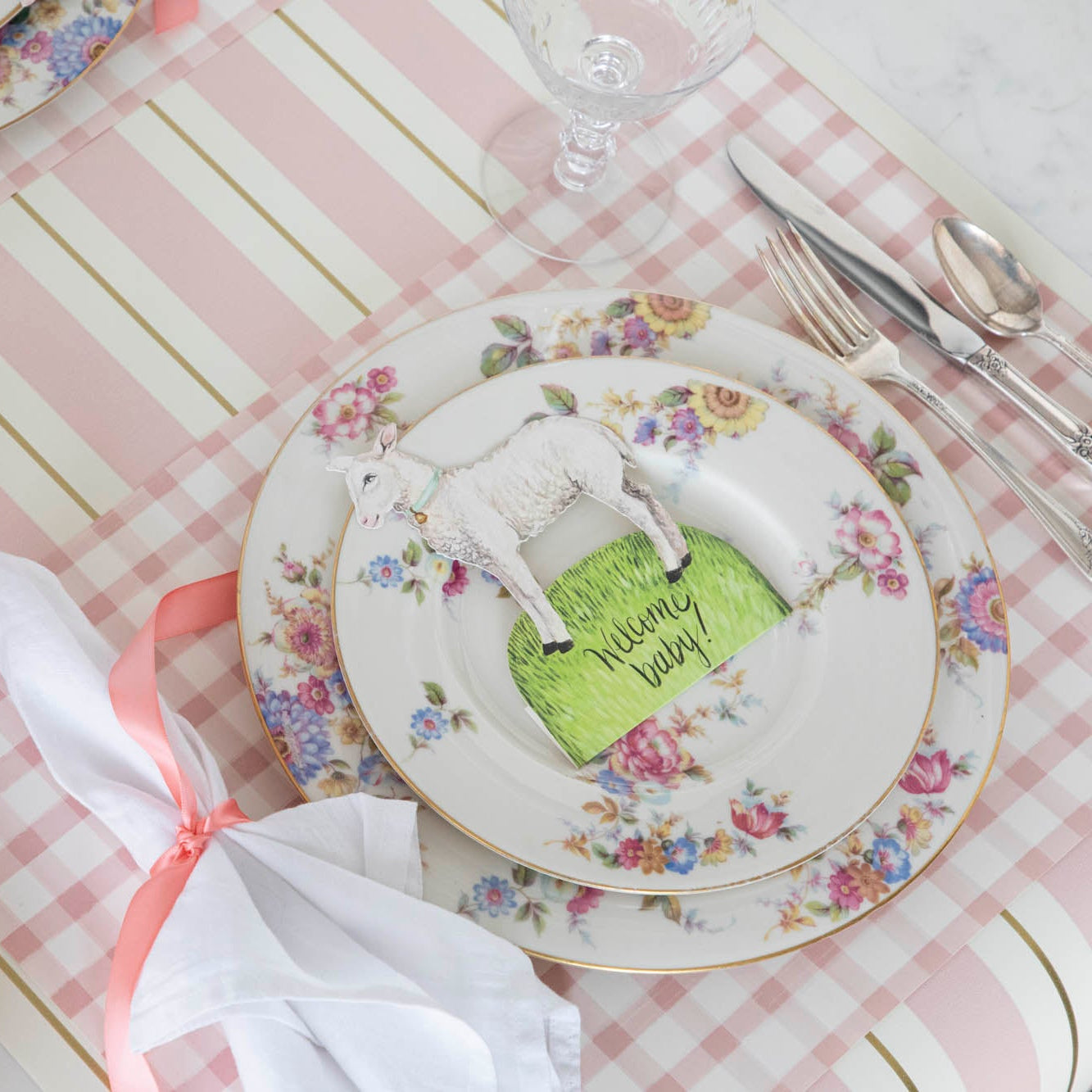 An Easter table setting with pink and white plates, napkins, and adorable Hester & Cook Little Lamb Place Card featuring an Easter Garden Story.