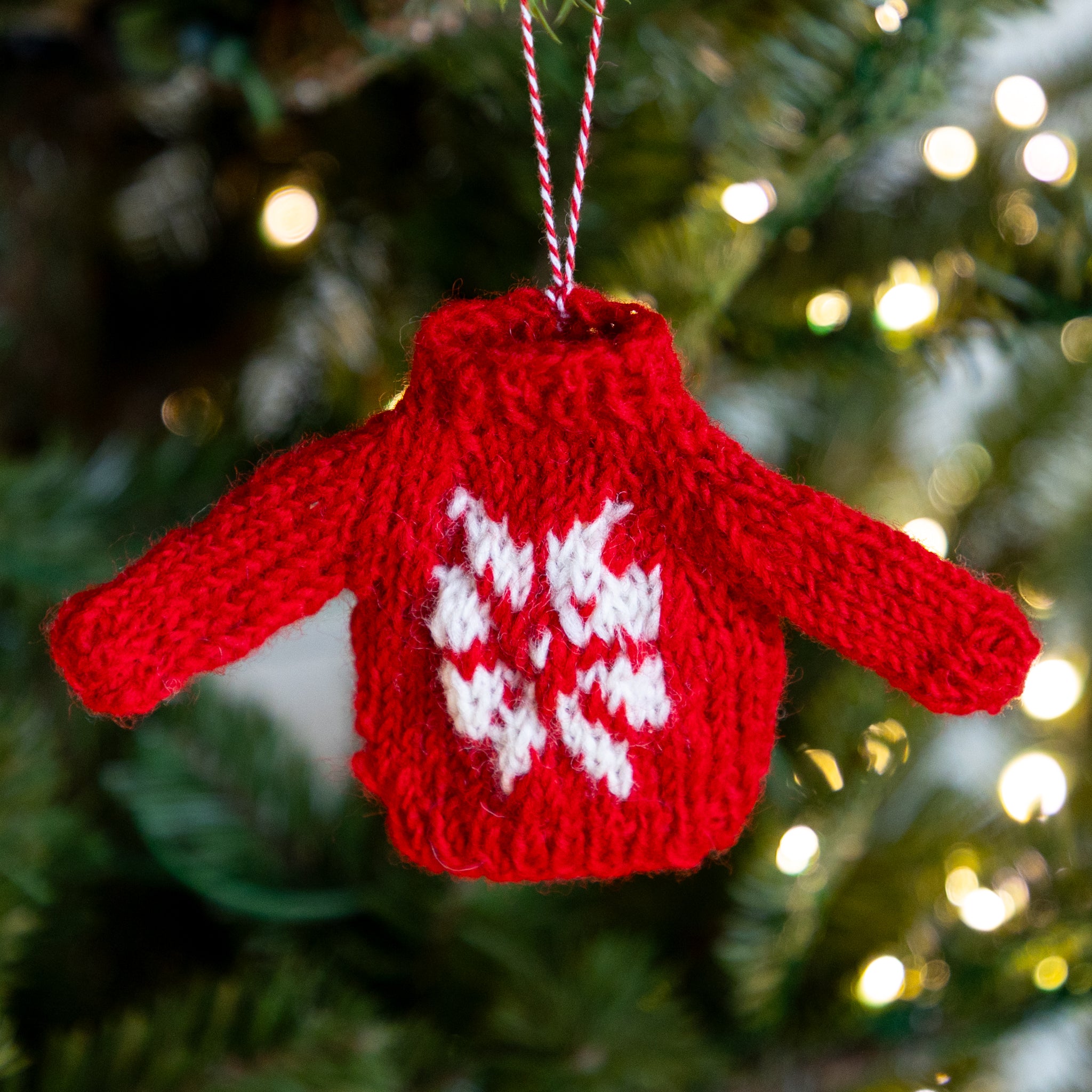 Red knitted sweater ornament with white snowflake design on a Christmas tree.