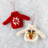 Two knitted sweater ornaments, one red with white snowflake pattern and the other cream with reindeer design, on a light gray background.
