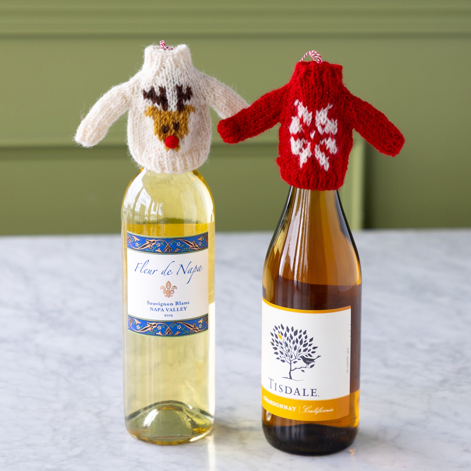 Two wine bottles with knitted sweaters on a light surface.