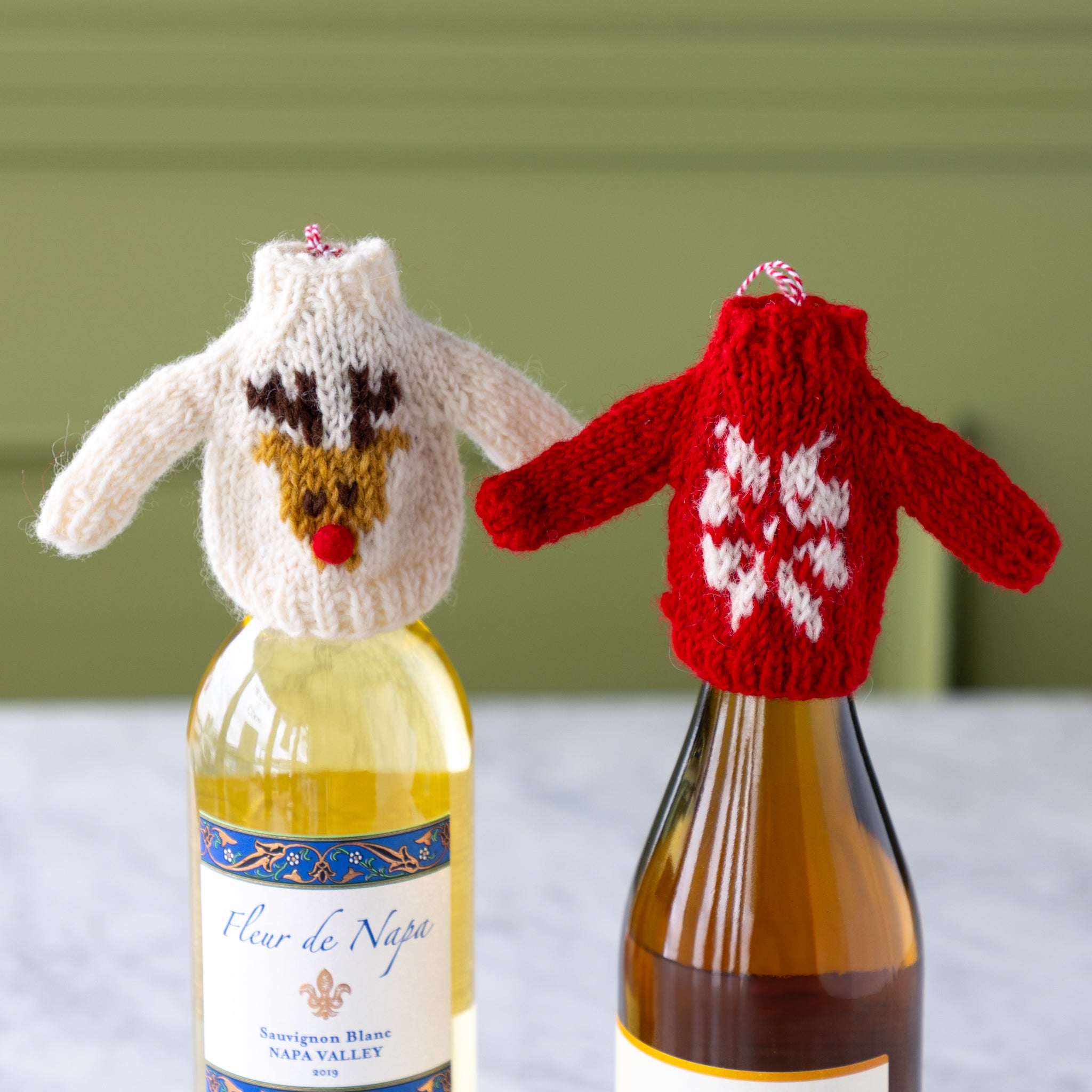 Two bottles of wine with knitted animal sweaters on a neutral background.
