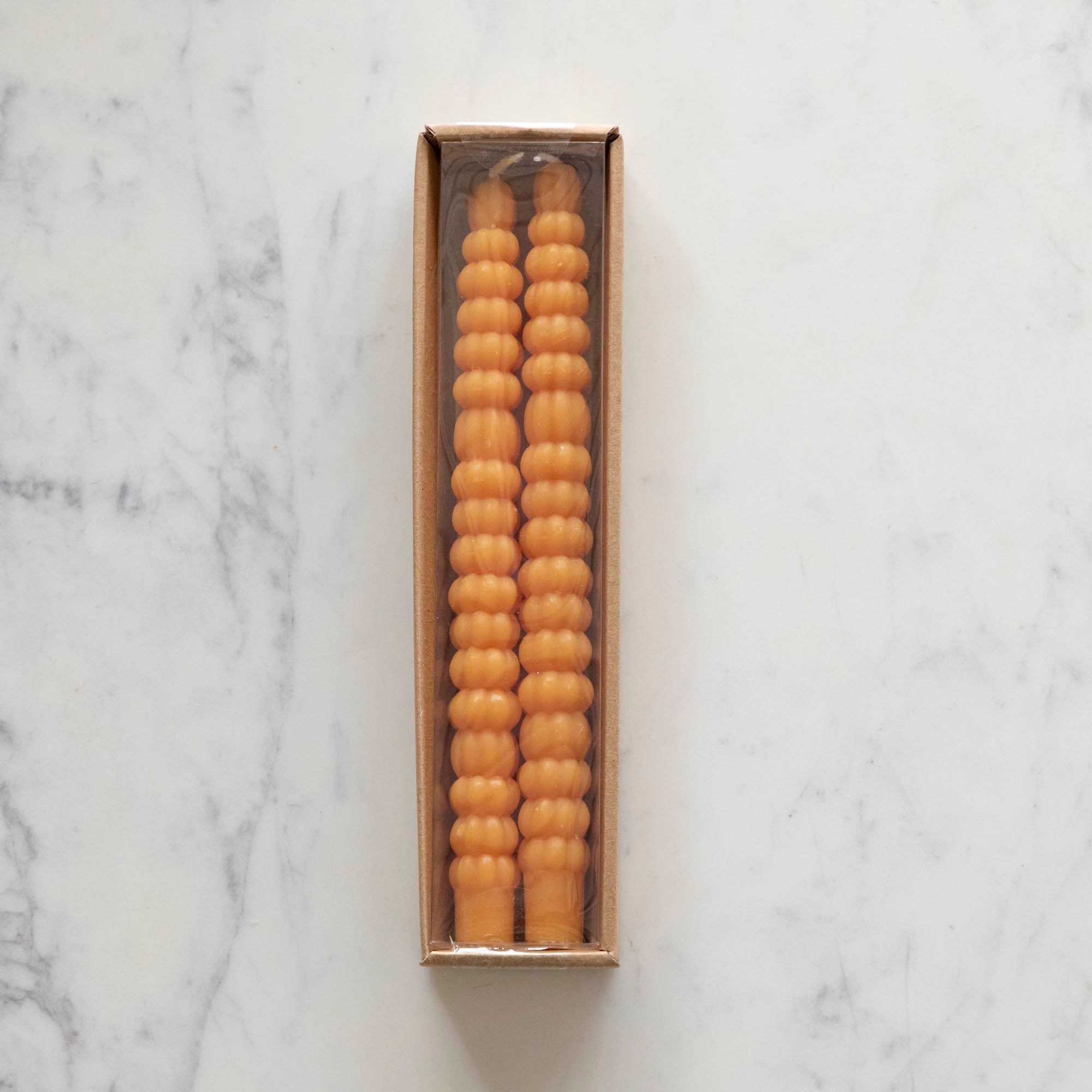 Two orange taper candles resembling stacks of tiny pumpkins laying in their package on a white table.