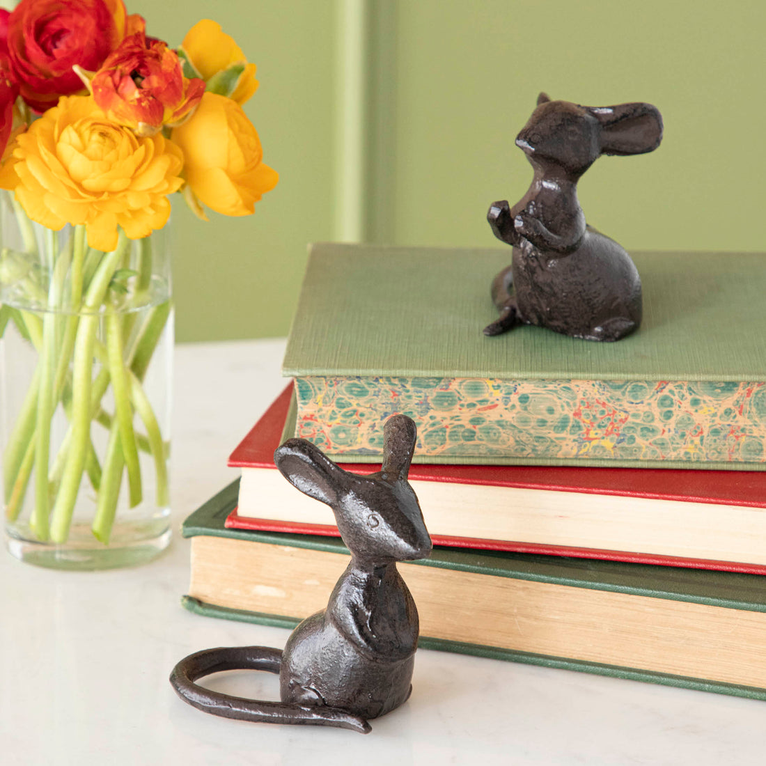 Two black cast iron mice figurines placed on top of a book next to a vase of flowers.