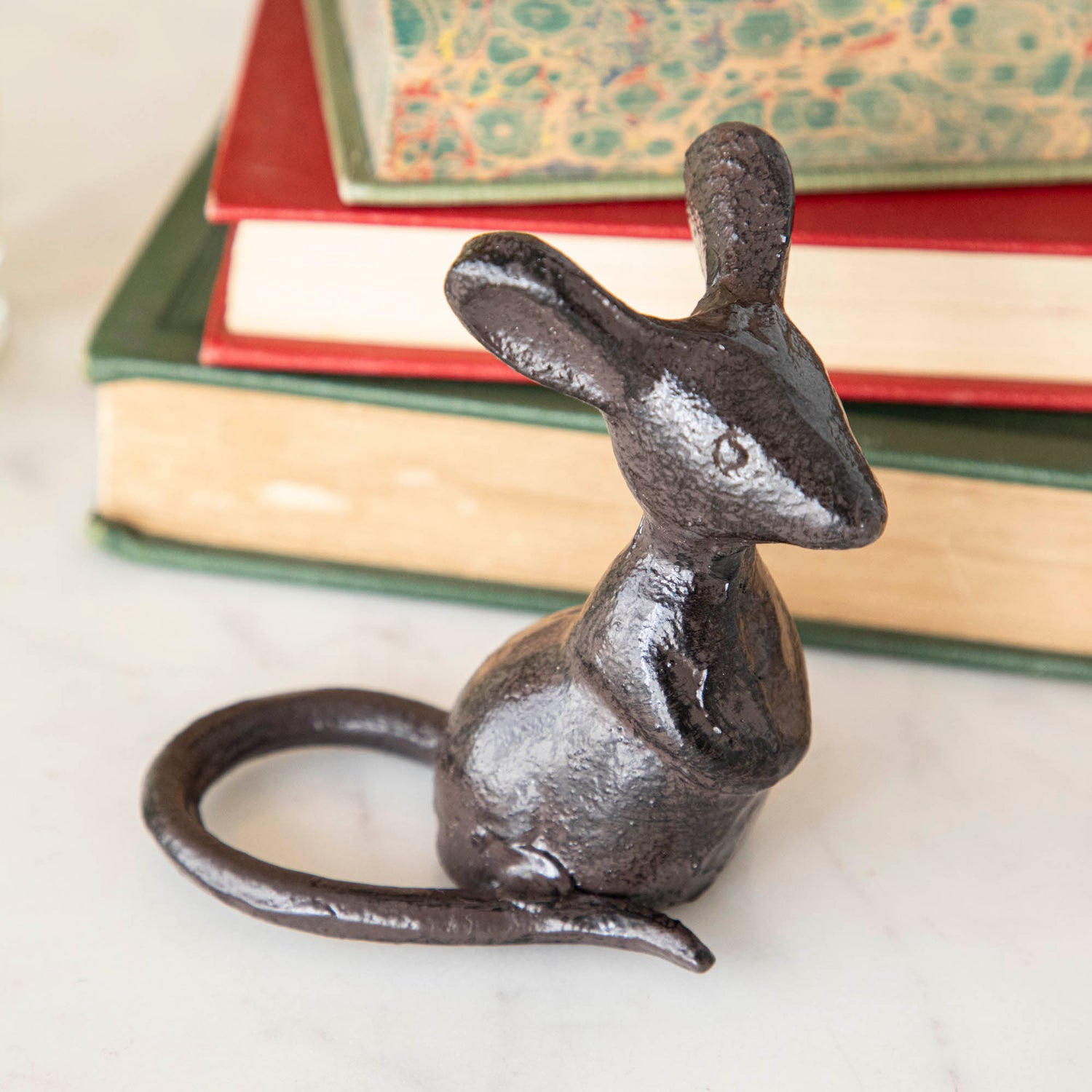 A cast iron mouse in front of a stack of books.