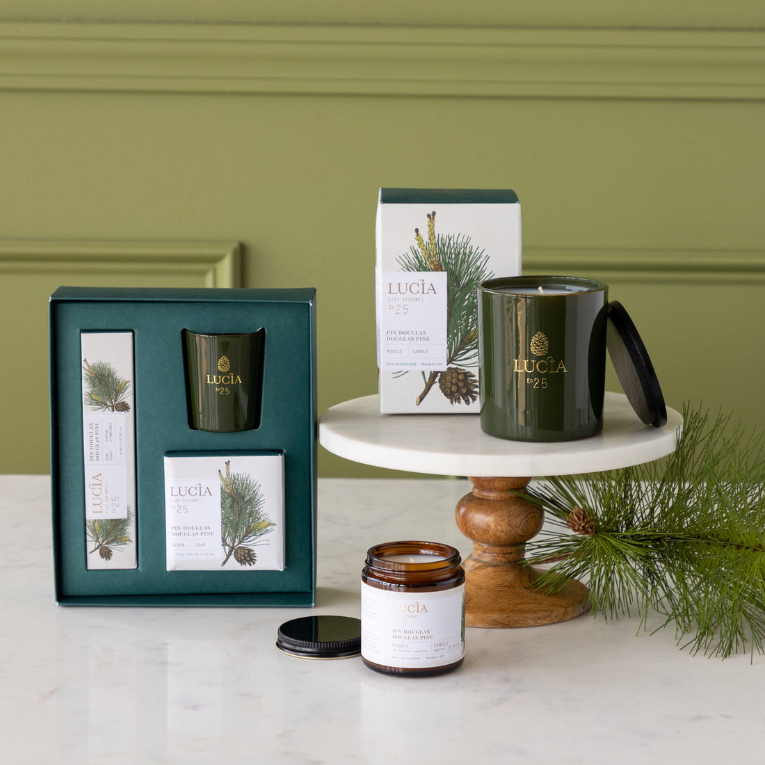 Candles and packaging with Lucia branding on a white surface against a green wall.